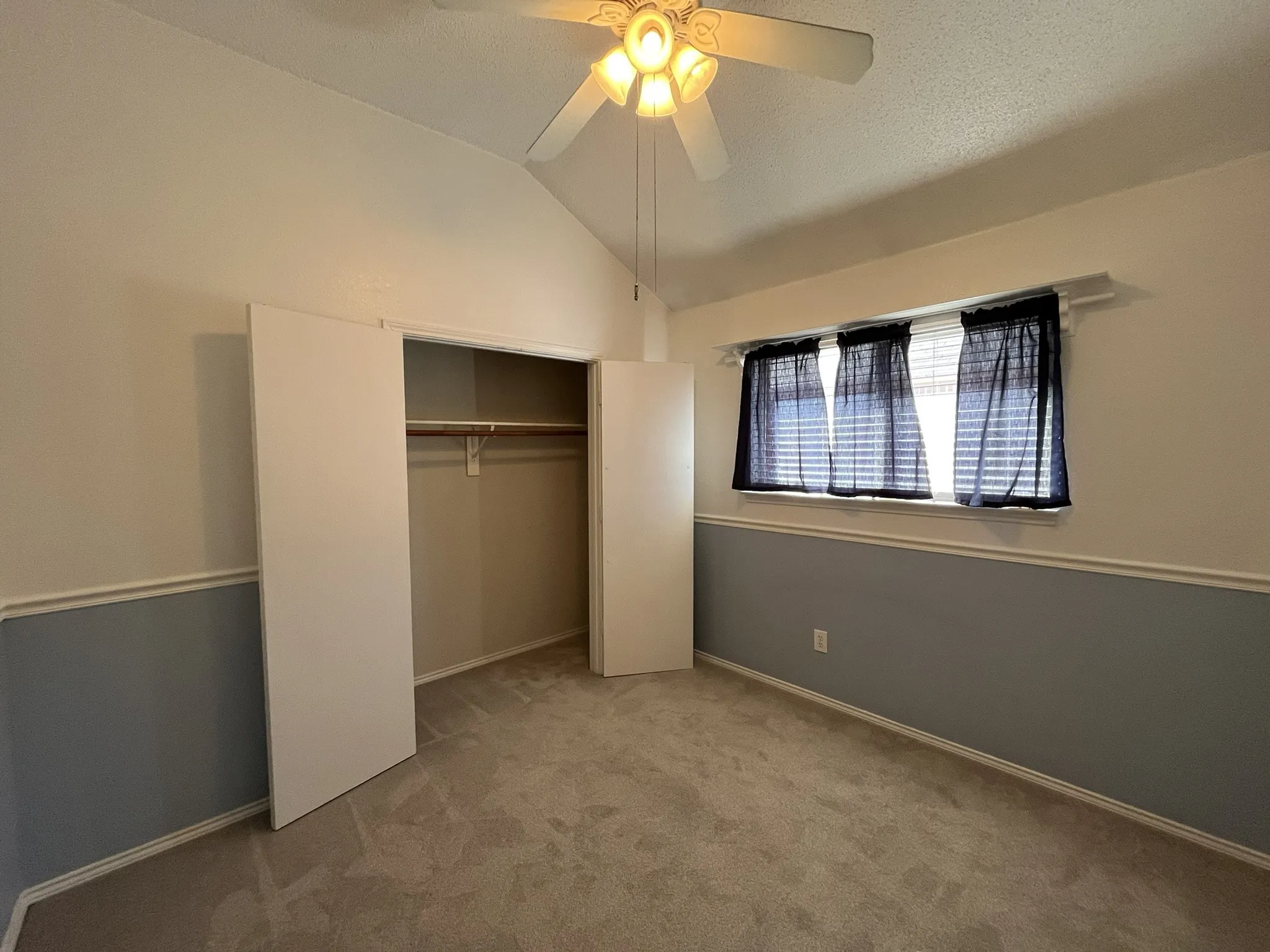 Vaulted ceiling with ceiling fan, wall-to-wall carpeting, window with blinds, and bi-fold closet doors with built-in shelving