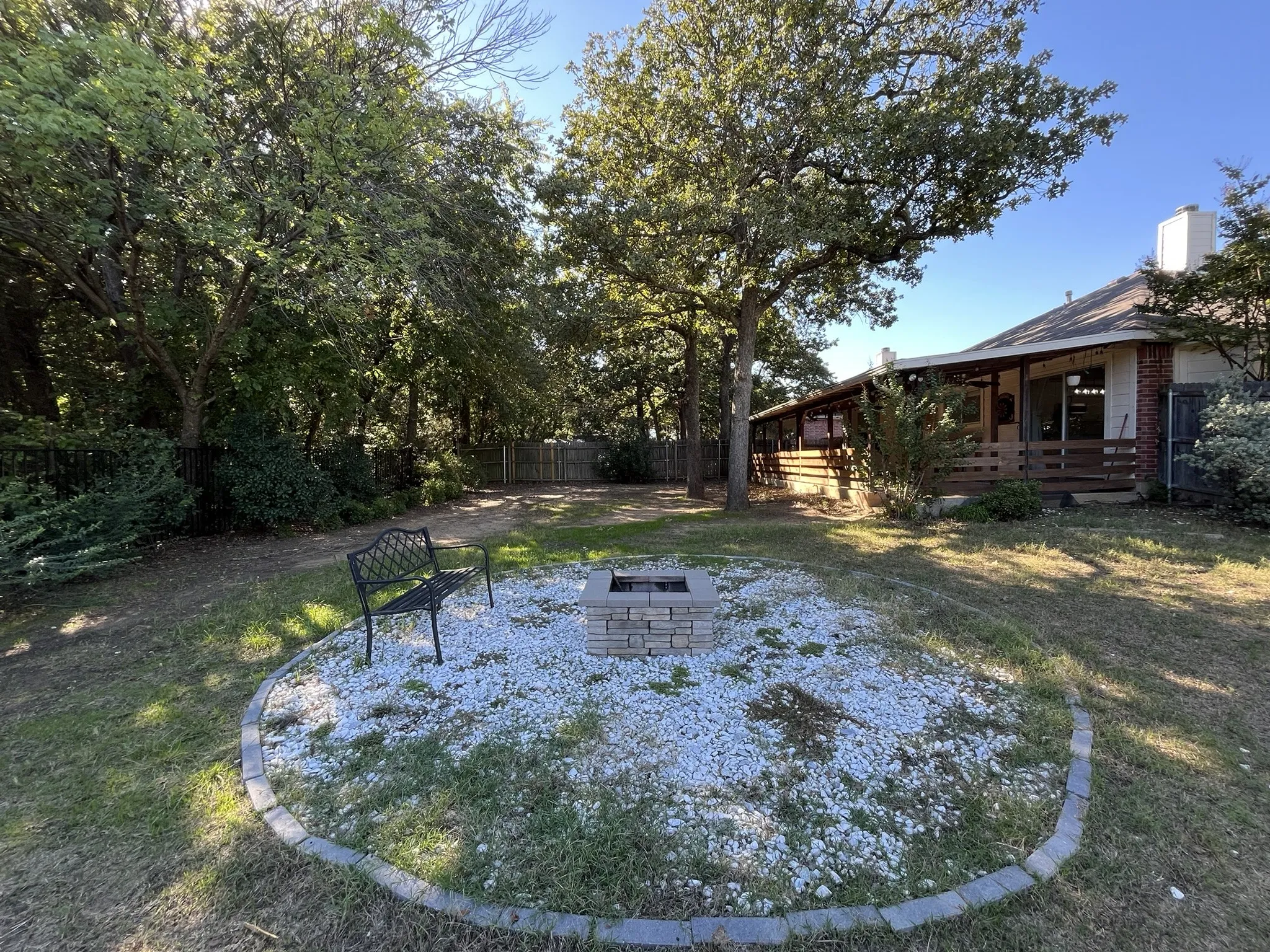 Backyard featuring a stone fire pit area, covered patio with wood railing, and mature trees