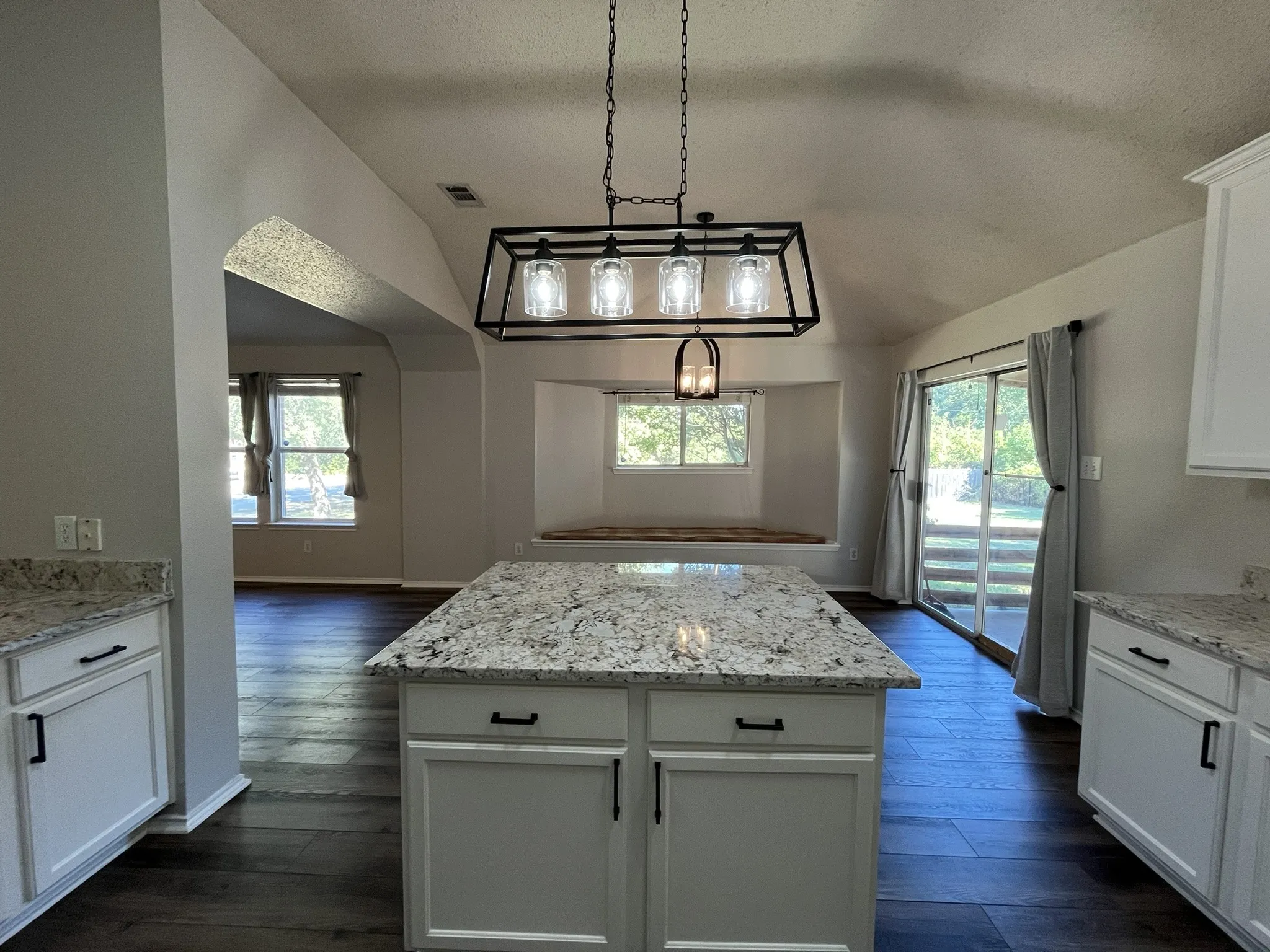 Kitchen island with granite countertop, white cabinetry, dark wood-finish flooring, and a sliding glass door