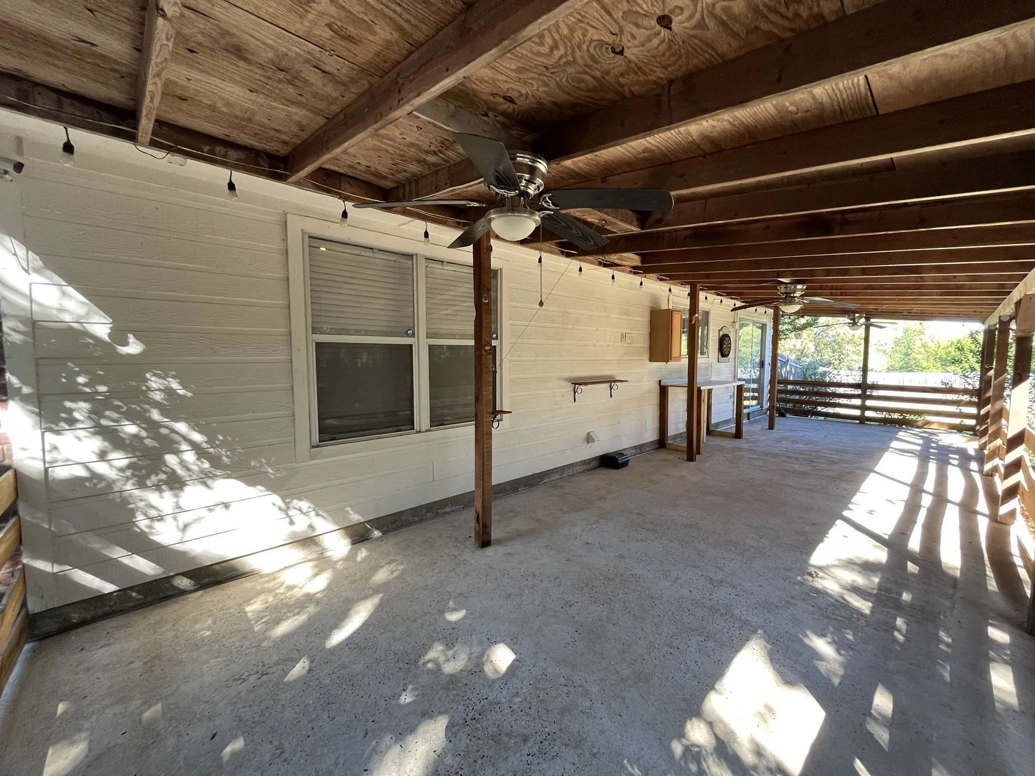 Spacious covered patio with concrete flooring, exposed wood beam ceiling, and two ceiling fans