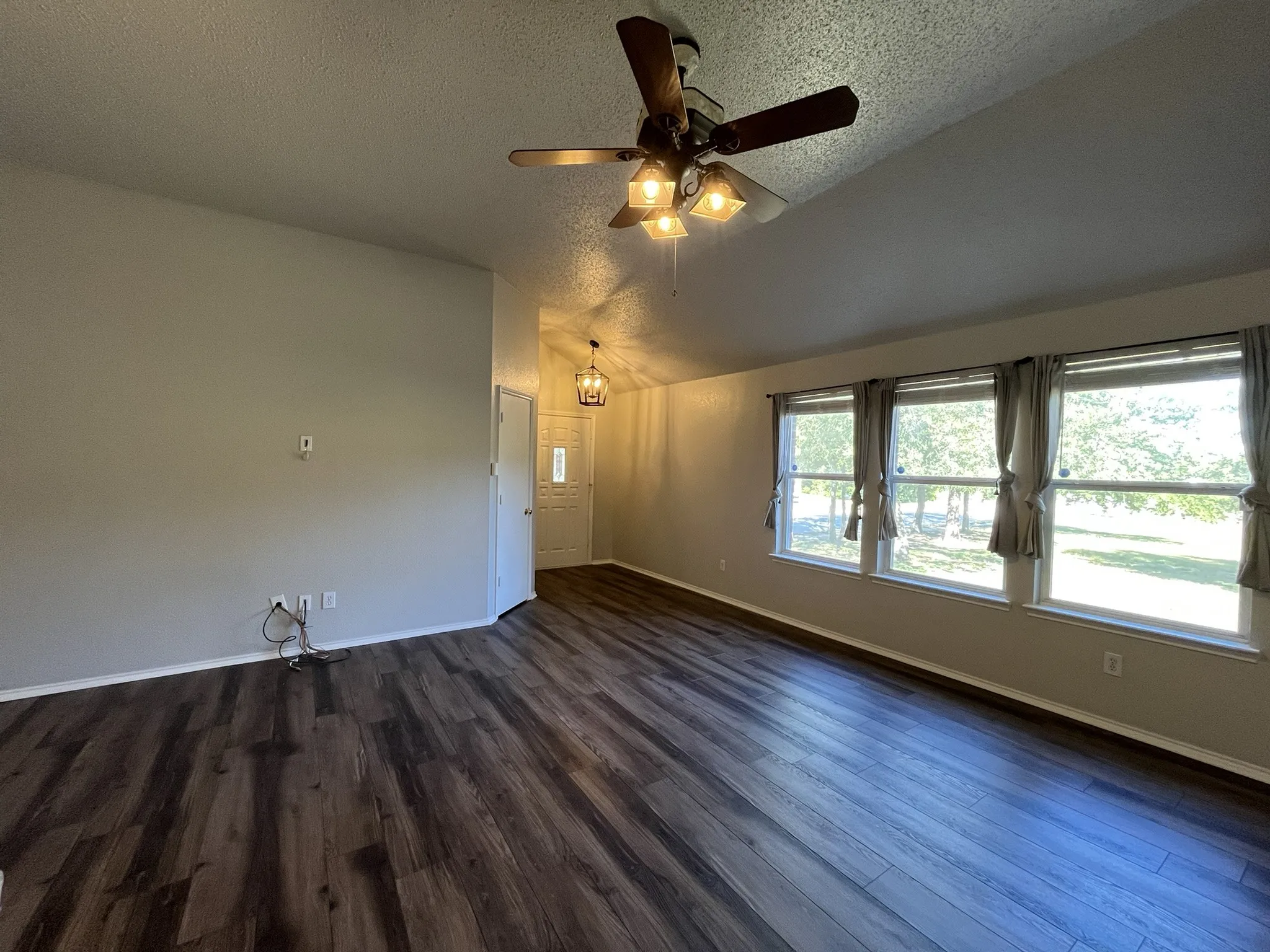 Vaulted ceiling, wood-finish flooring, ceiling fan with light fixture, multiple windows, and a built-in light fixture