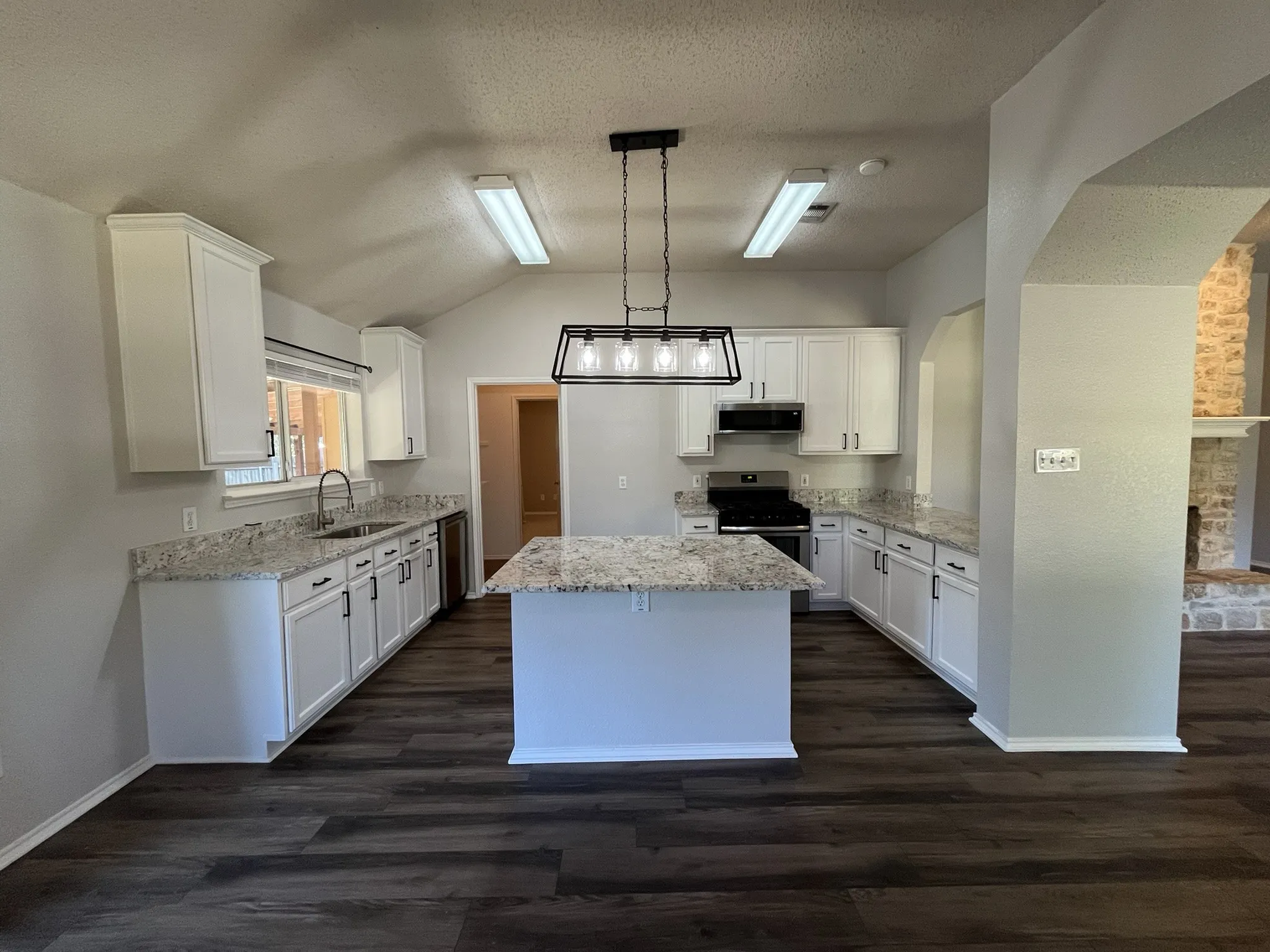 Kitchen featuring white cabinetry, light-toned countertops, a center island, wood-finish flooring, and a vaulted ceiling