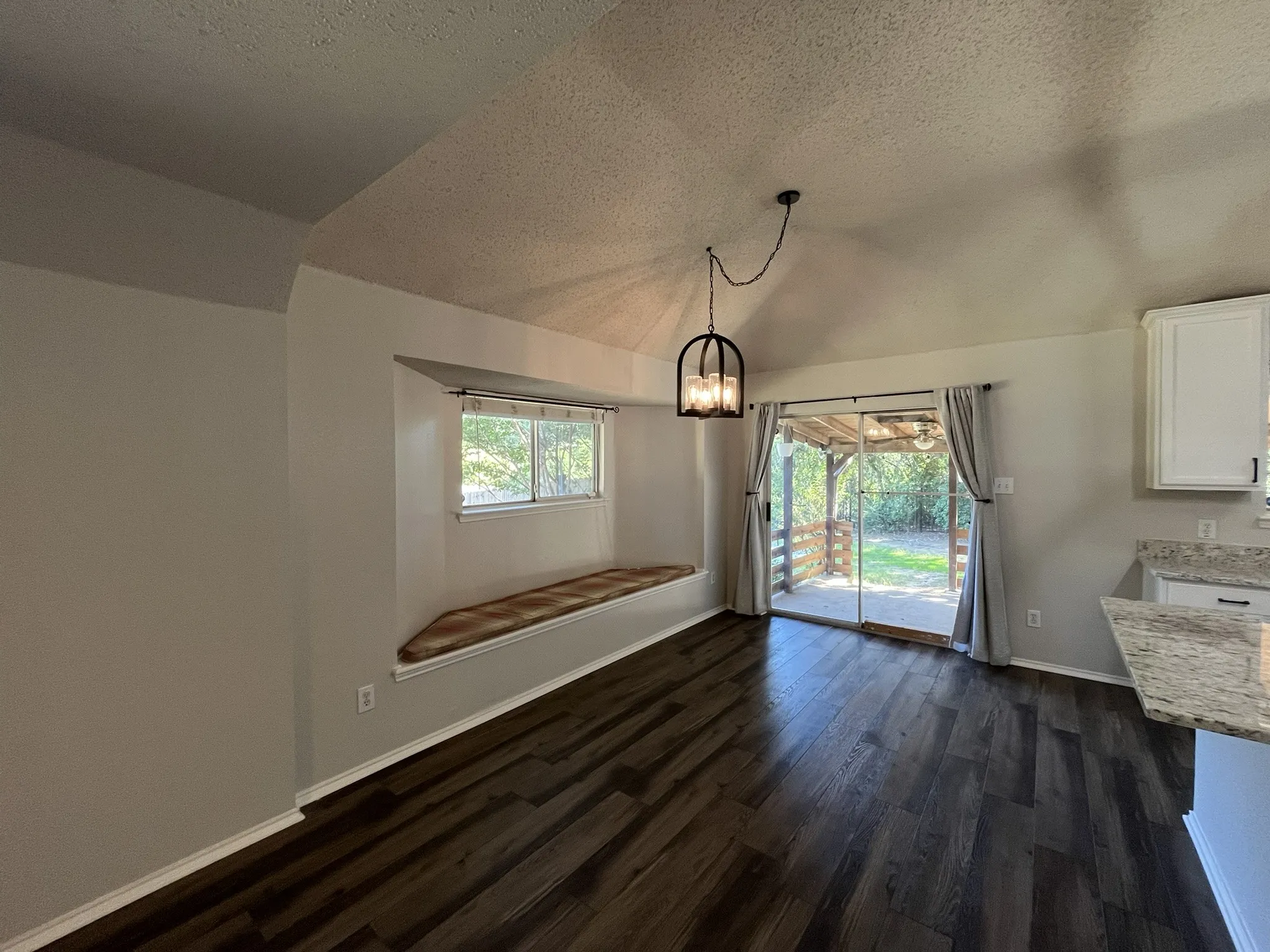 Vaulted ceiling with a pendant light fixture, wood-finish flooring, built-in window seat, and sliding glass doors opening to an outdoor area