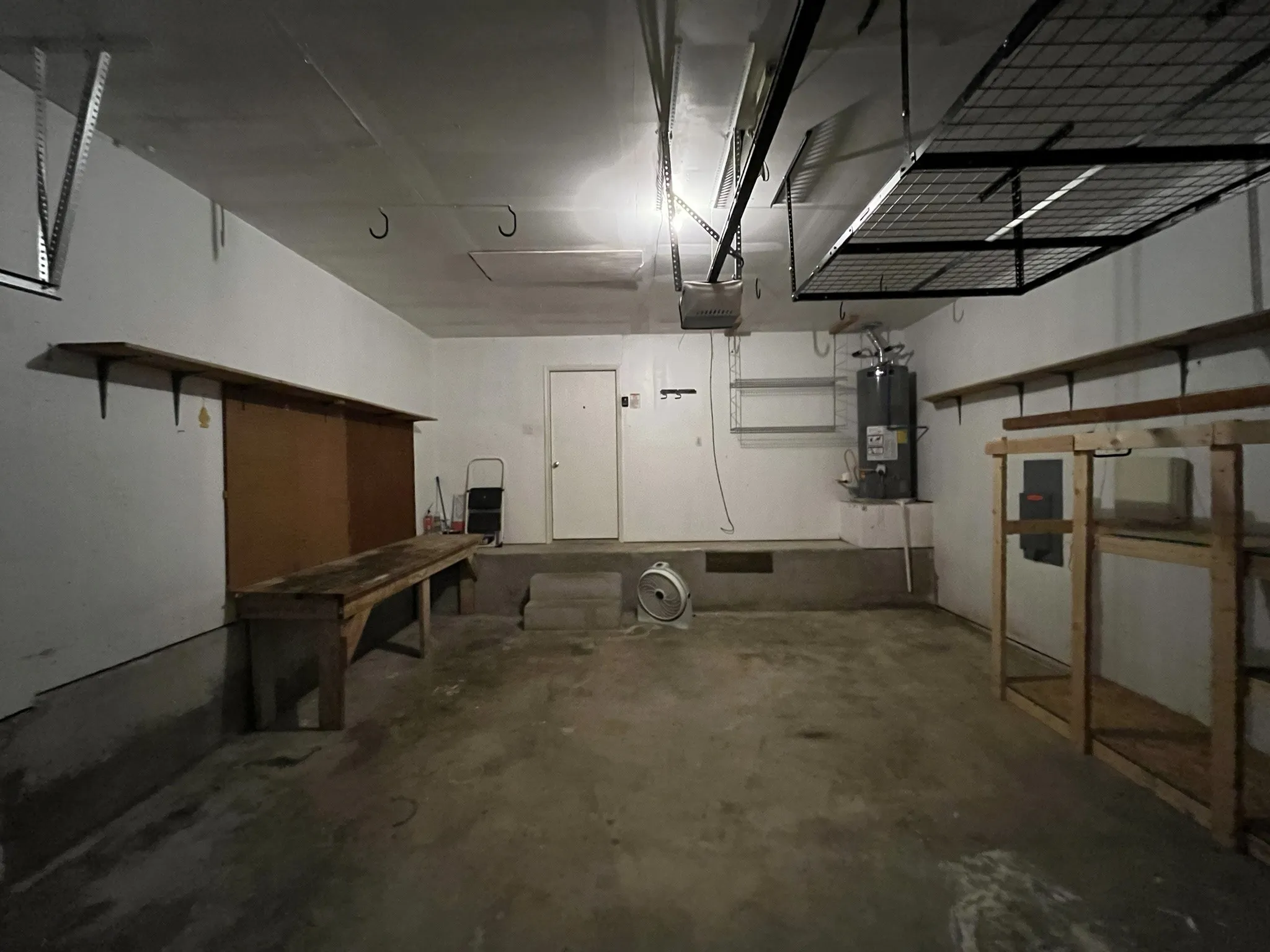 Attached garage with concrete flooring, built-in shelving, overhead storage racks, and a water heater