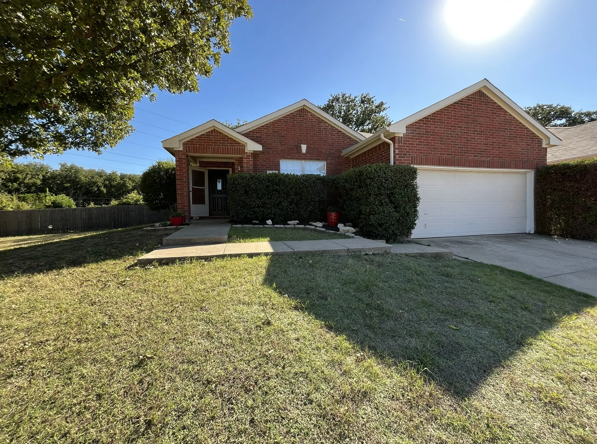 Brick exterior, attached garage, covered entryway, concrete driveway, and mature landscaping