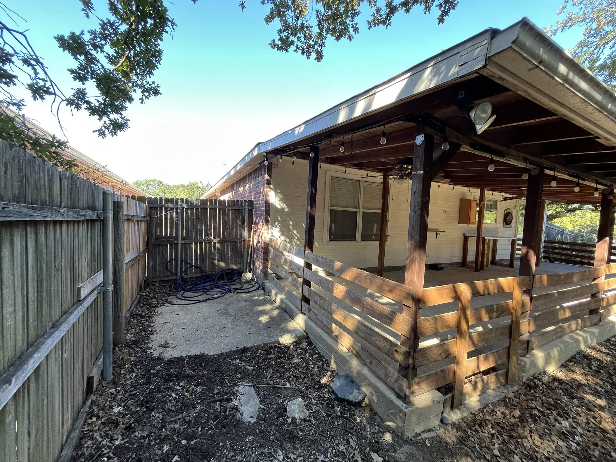 Covered outdoor patio with exposed wood beams and string lighting, featuring a wood-slat railing