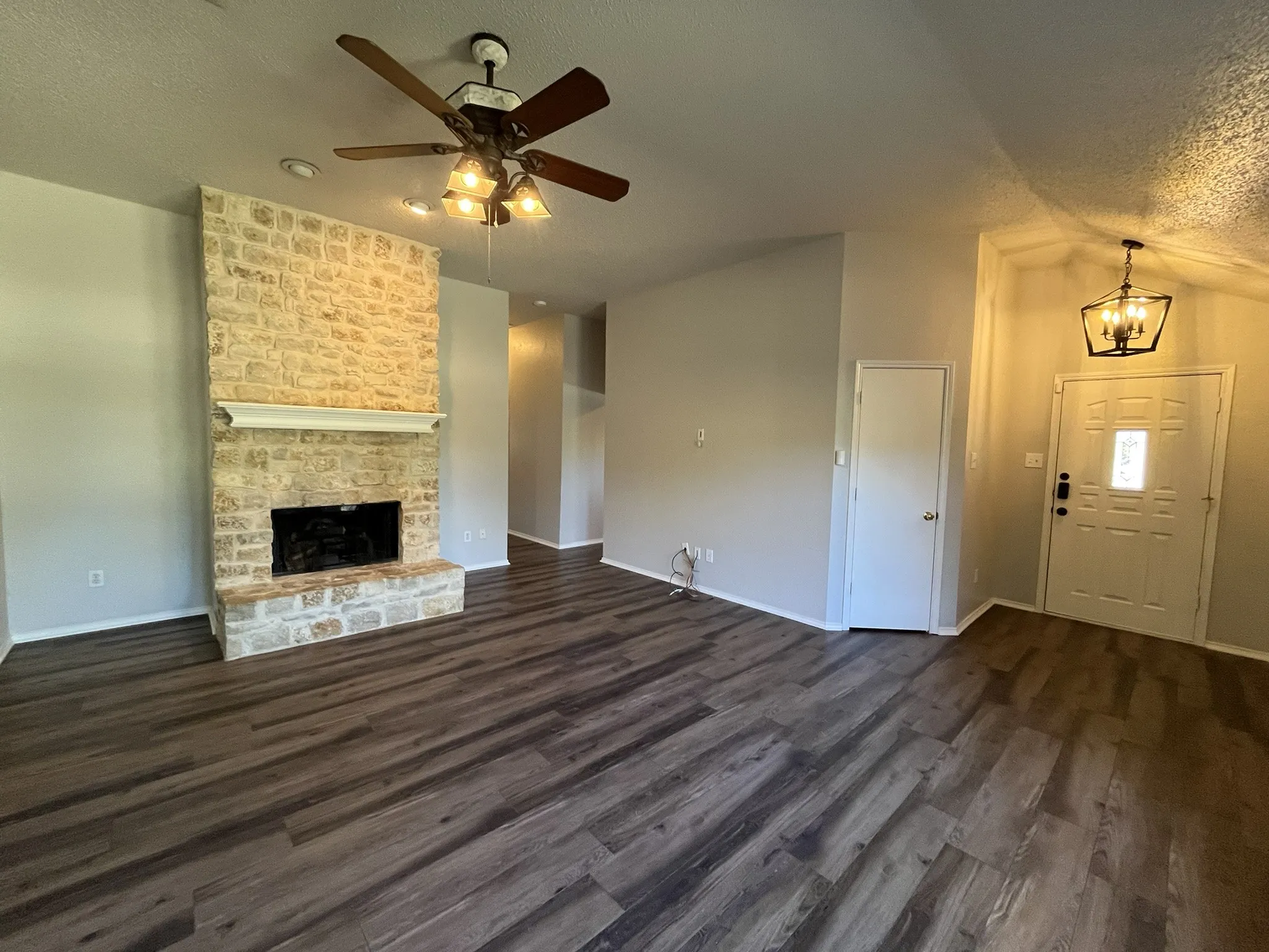 Stone-clad fireplace with mantel, dark wood-finish flooring, ceiling fan with integrated lighting, and vaulted ceiling