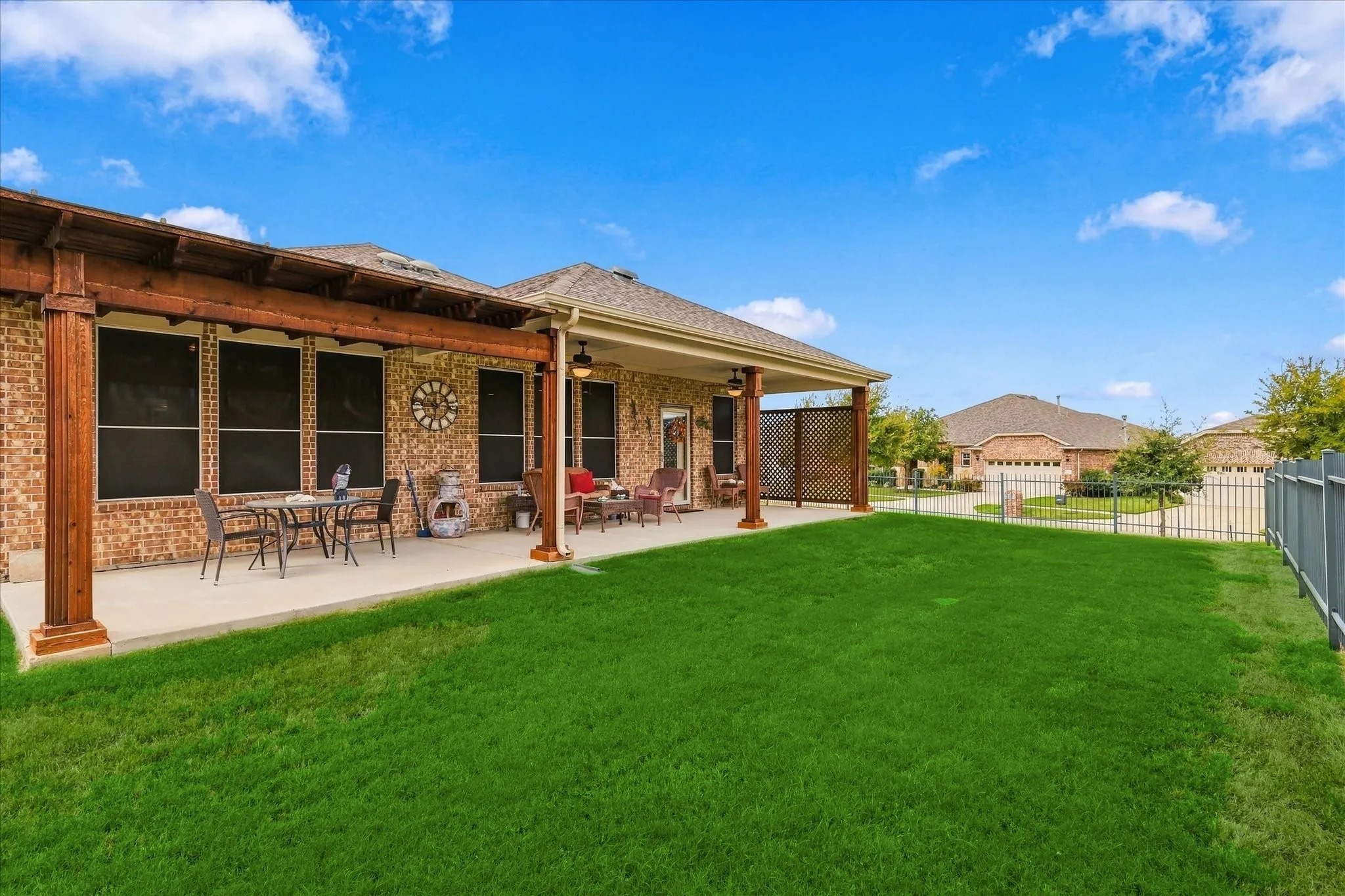Covered patio featuring a timber-frame pergola, concrete flooring, exterior brick masonry, and metal fencing