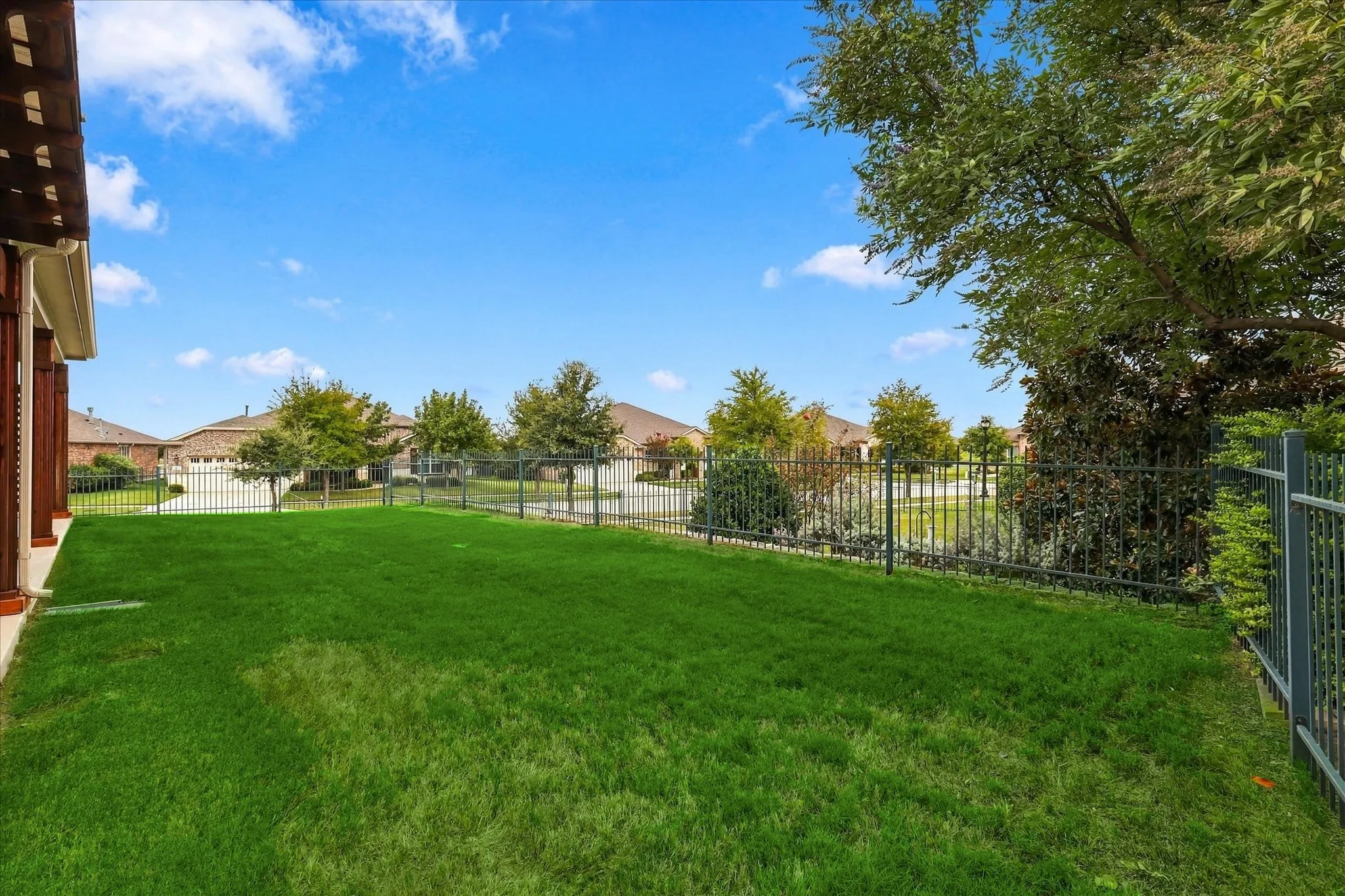 Fully Fenced backyard featuring a manicured lawn, perimeter metal fencing, and mature trees