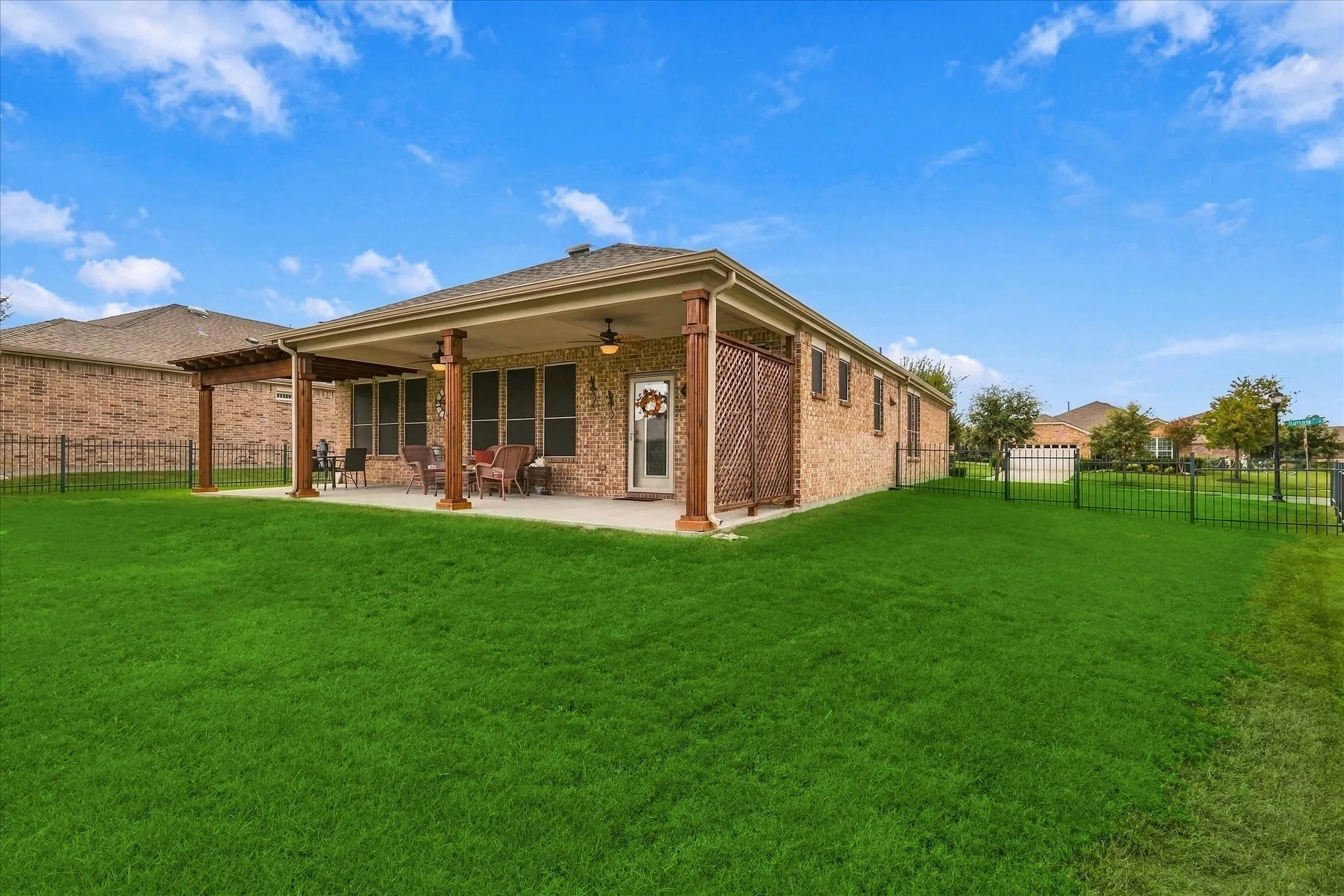 Brick exterior featuring a covered patio, wooden support columns, lattice privacy screening, and a fenced yard