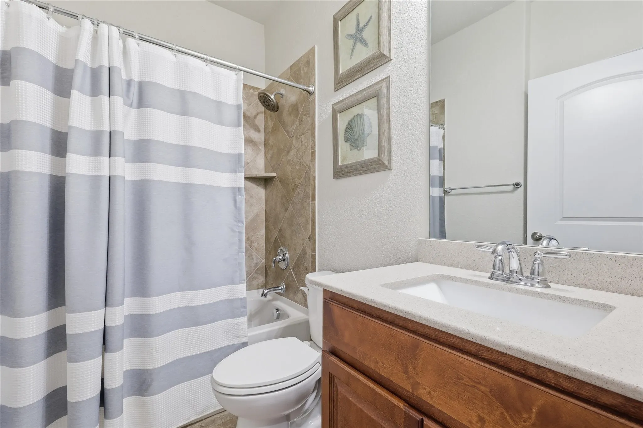 Bathroom featuring a wood-finish vanity with Quartz countertop, an integrated rectangular sink, tile surround in the tub-shower combination, and a large wall-mounted mirror
