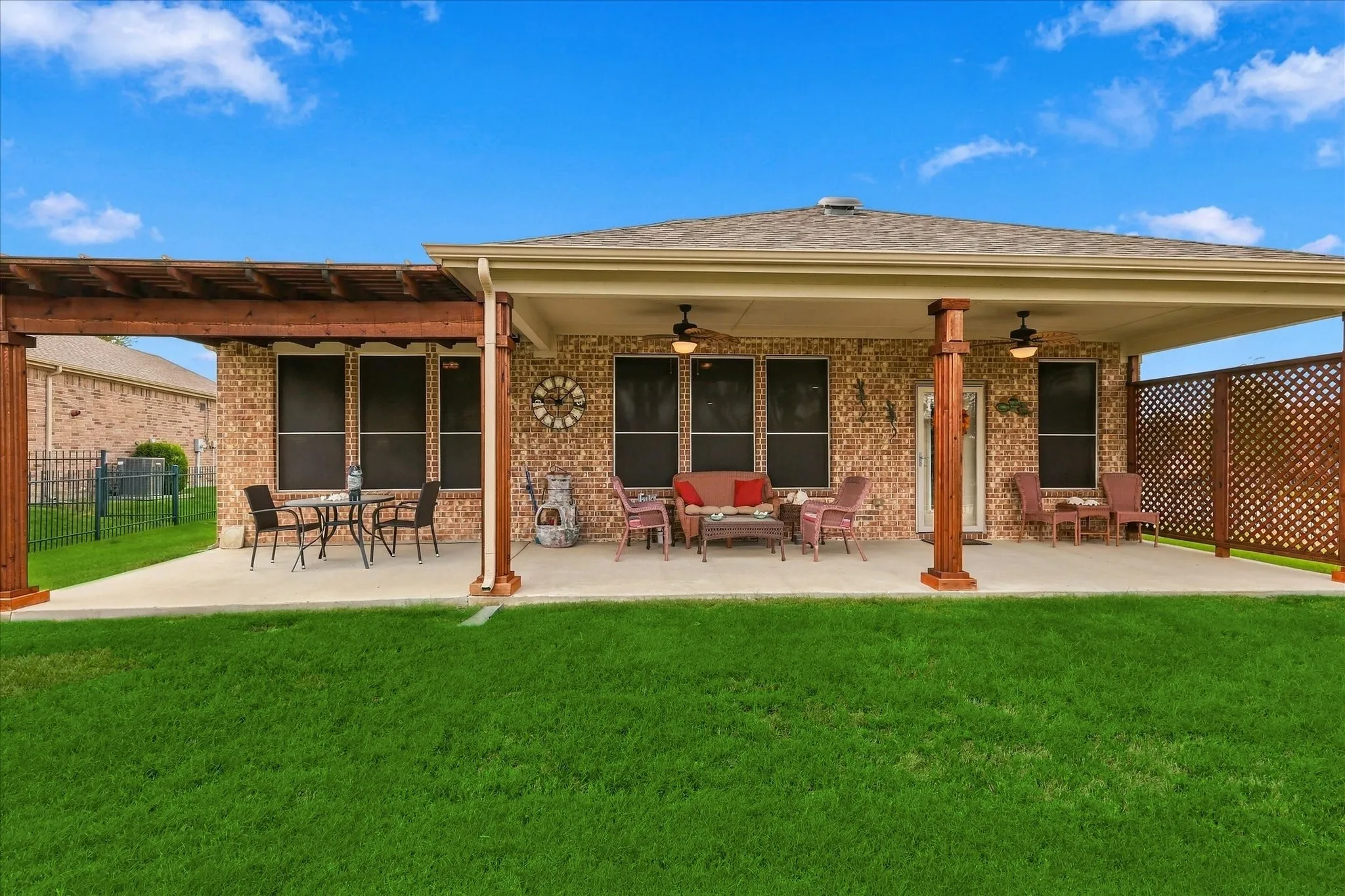Brick exterior patio featuring a covered area with recessed lighting, integrated ceiling fans, a wood-beam pergola extension, and wood-lattice privacy screening and fully fenced backyard