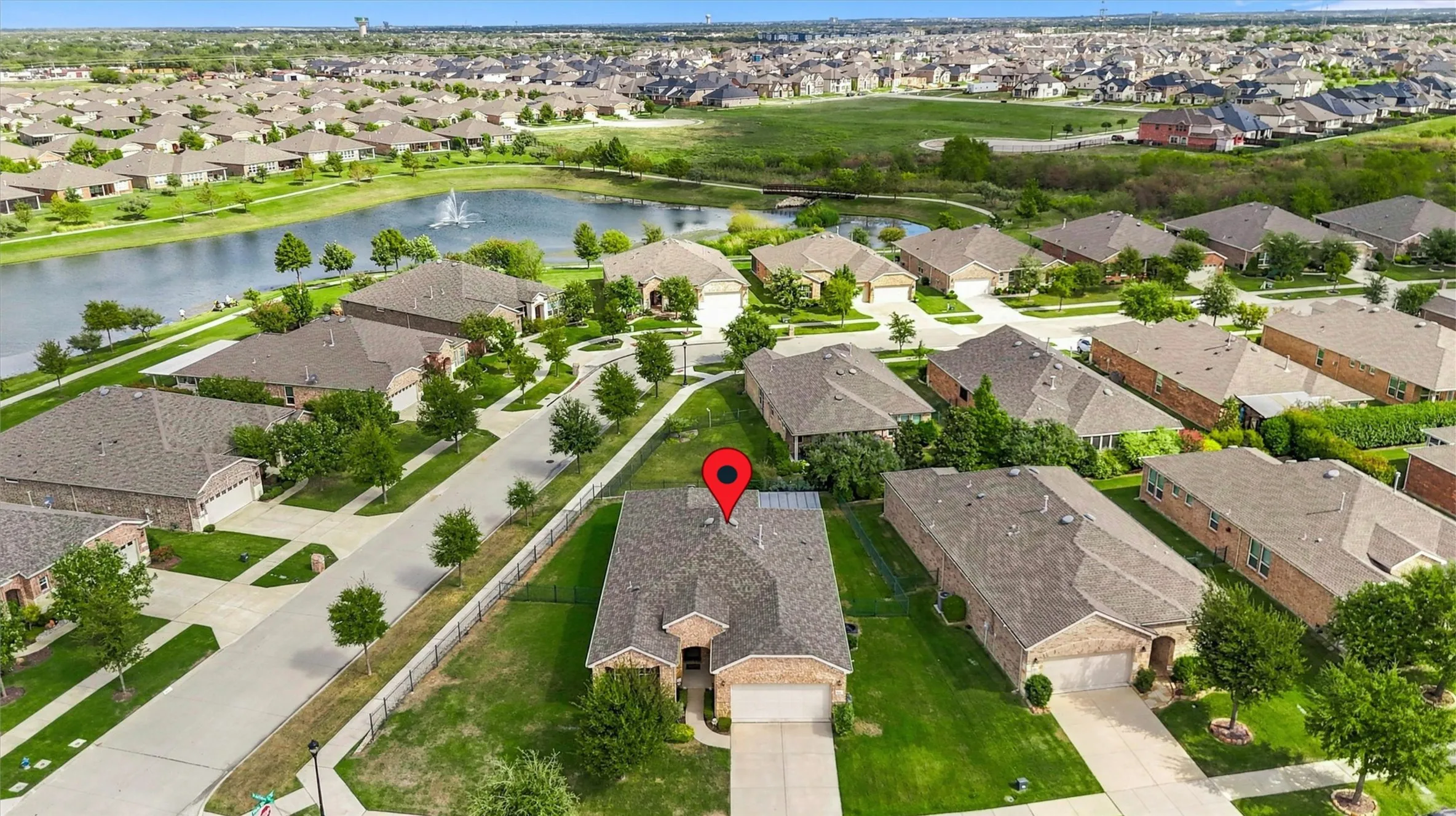 Aerial perspective of a brick-exterior residence featuring an attached two-car garage, expansive lawn, and proximity to a community pond