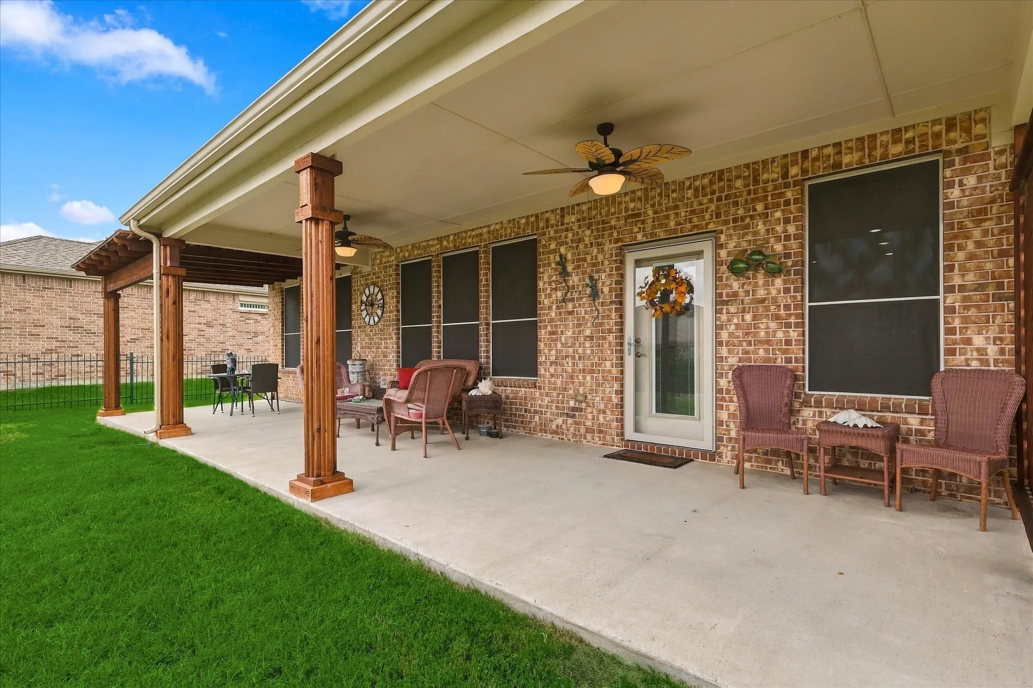Covered patio featuring a concrete floor, brick exterior wall, wood-finish support columns, a timber pergola extension, and ceiling-mounted fans
