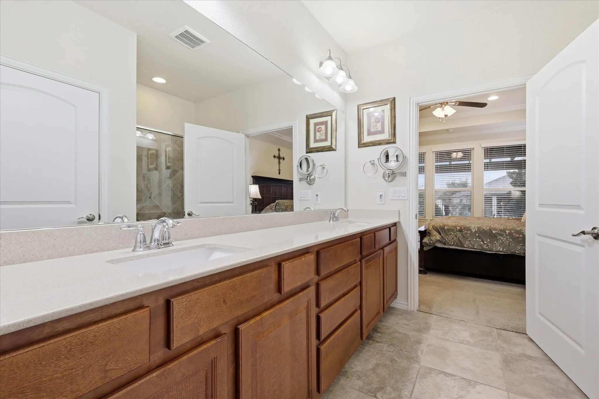 Double vanity featuring stained wood cabinetry, stone-finish countertops, undermount sinks, and a full-width wall mirror