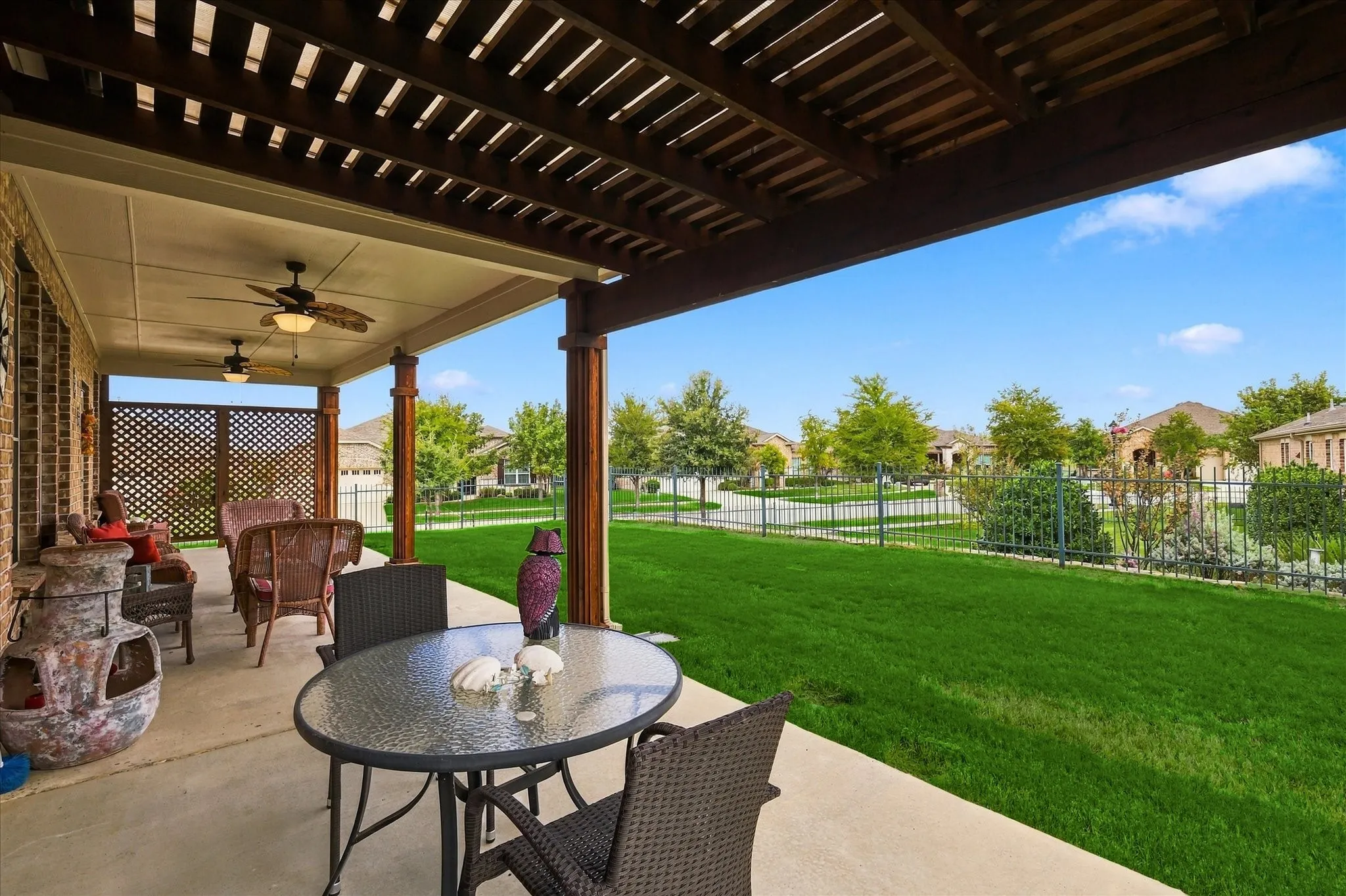 Covered concrete patio featuring a timber pergola, wood-column supports, and dual ceiling fans, spanning a fenced backyard with a lawn