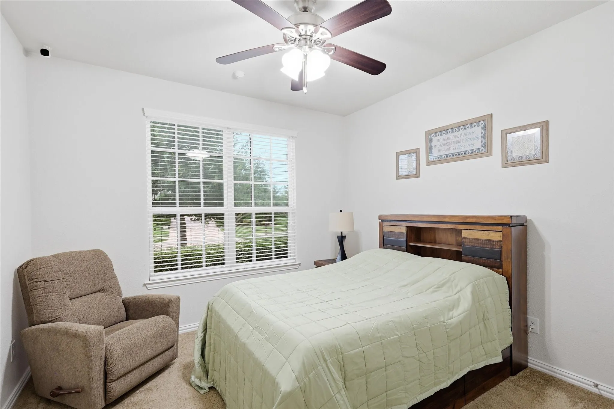 Neutral wall finishes, multi-pane window with horizontal blinds, ceiling fan with integrated lighting, and neutral carpeting