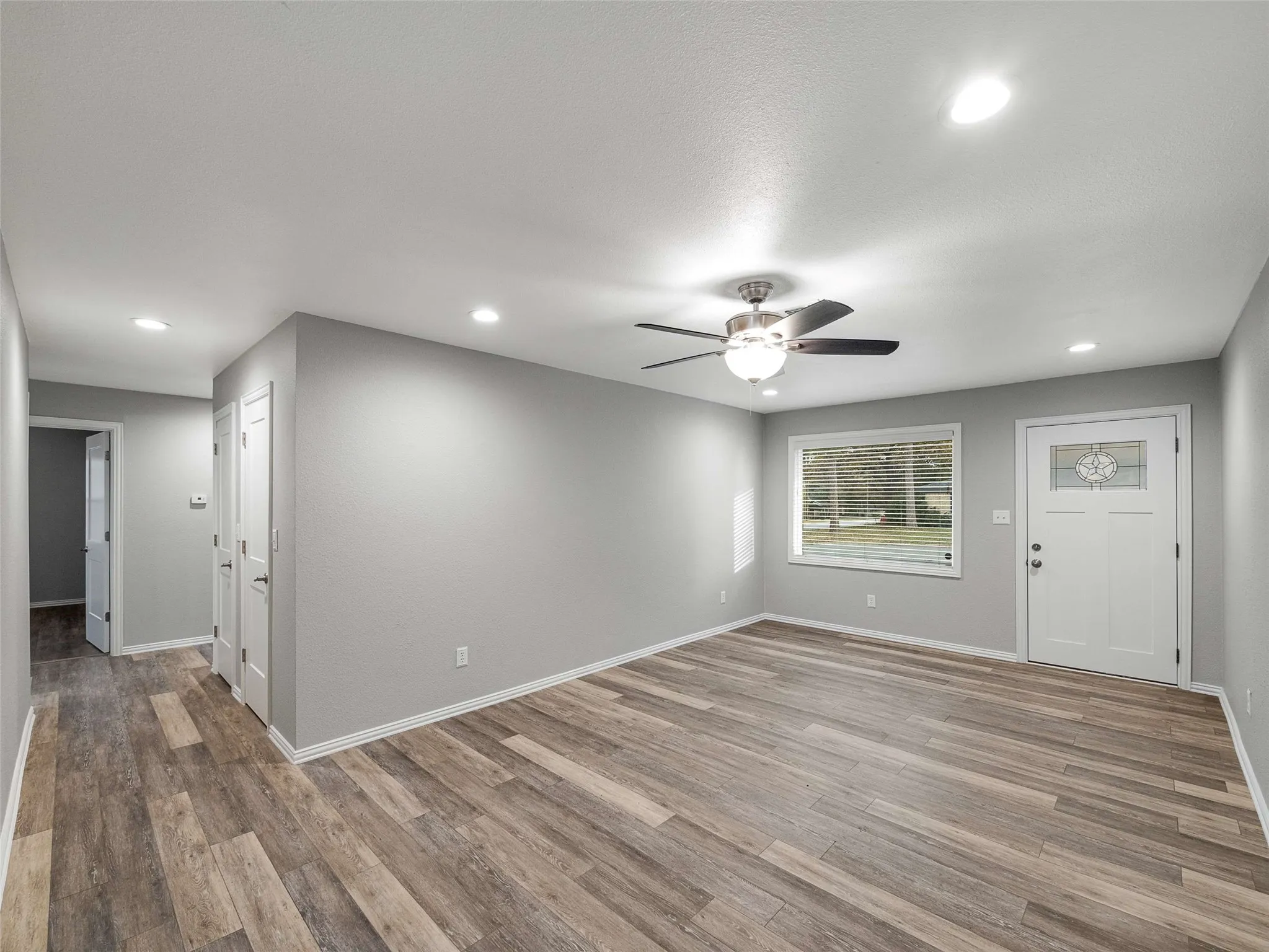 Wood-finish flooring, neutral interior paint, recessed lighting, ceiling fan with light fixture, and an exterior door featuring a decorative glass insert
