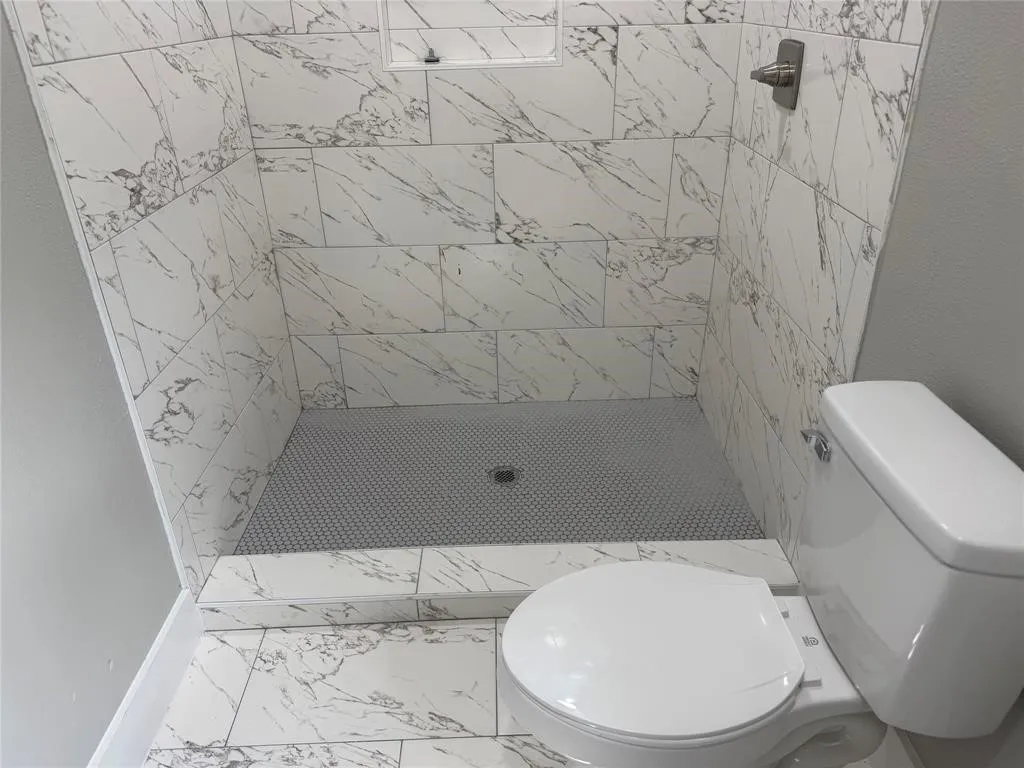 Walk-in shower featuring large-format patterned wall tile, a recessed niche, a textured mosaic tile floor, and a metal shower control