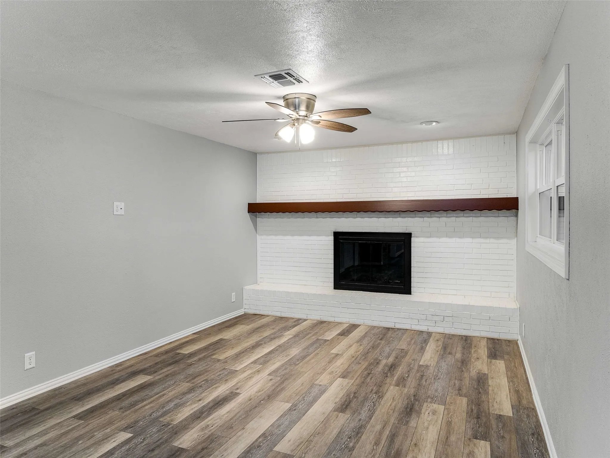 Painted brick fireplace surround featuring a wood-finish mantel and a raised hearth, complemented by wood-finish flooring and a multi-blade ceiling fan
