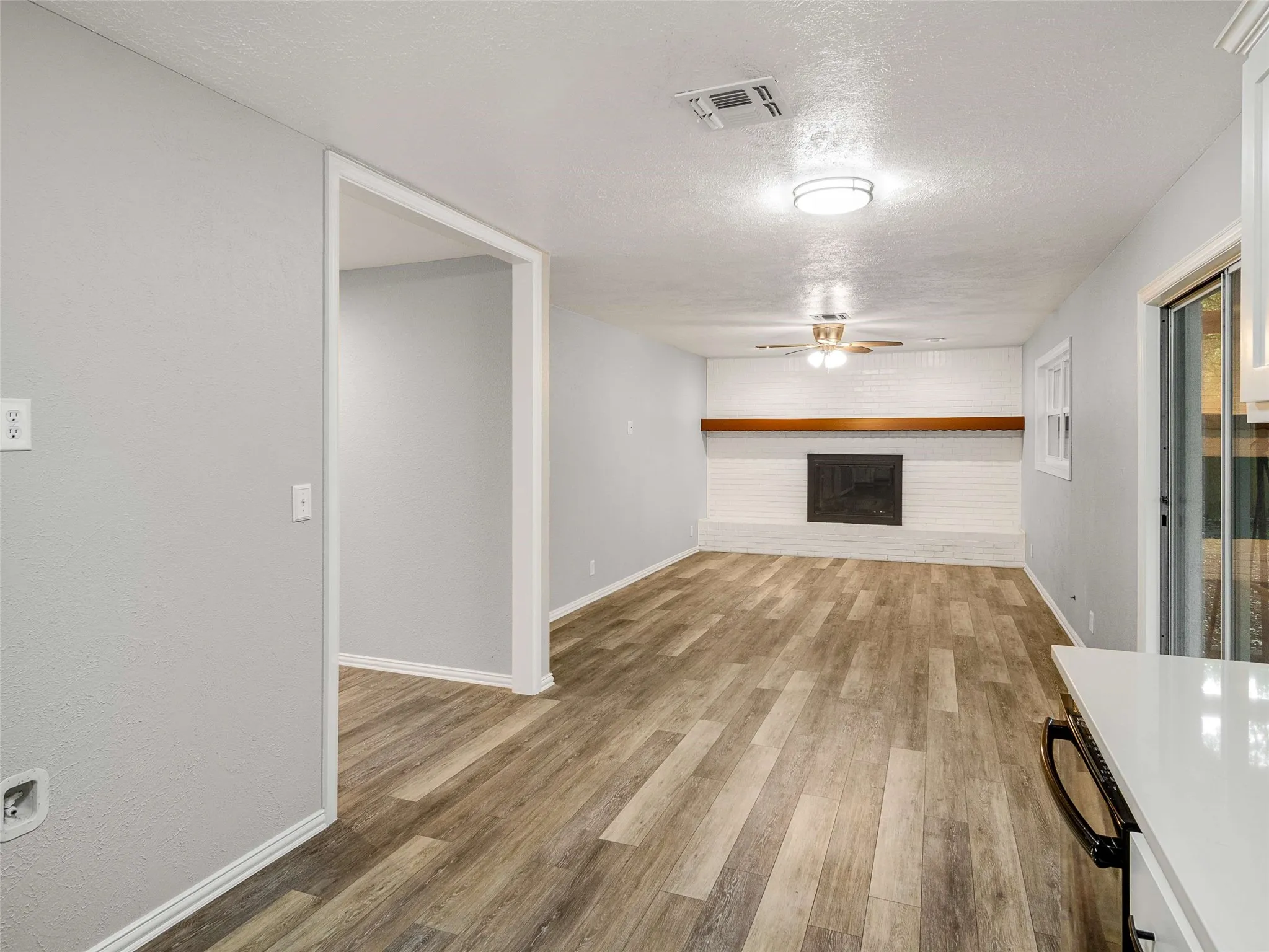 Living area featuring wood-finish flooring, a painted brick fireplace with a wood mantel, a ceiling fan, and sliding glass doors