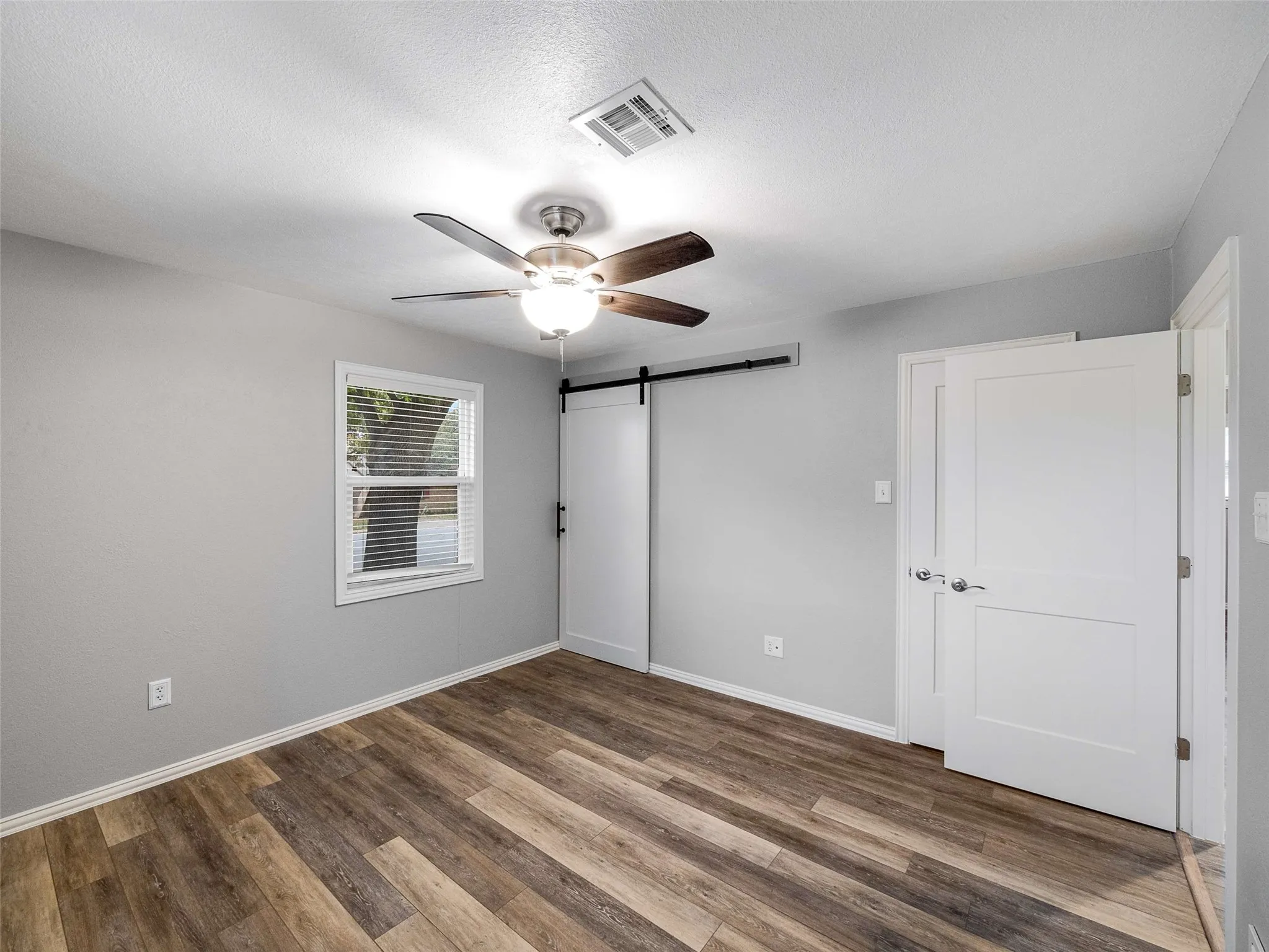 Room featuring wood-finish flooring, a sliding barn door with black hardware, a ceiling fan with integrated light fixture, and two-panel interior doors