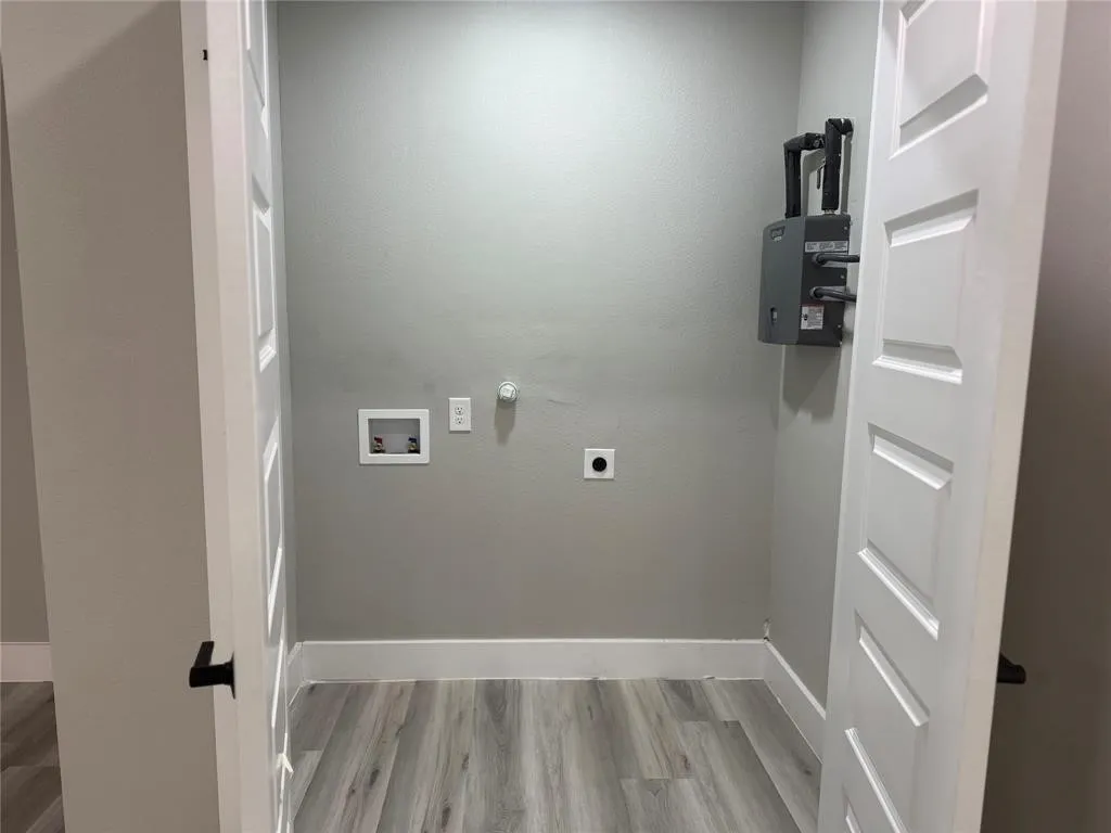 Utility closet featuring wood-finish flooring, white paneled doors, and wall-mounted tankless water heater