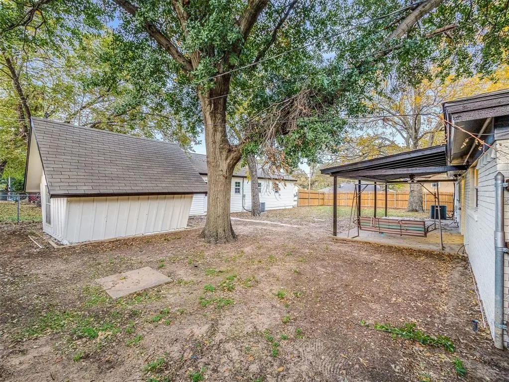 Backyard featuring a detached storage structure, mature trees, a covered patio with a ceiling fan, and wooden perimeter fencing