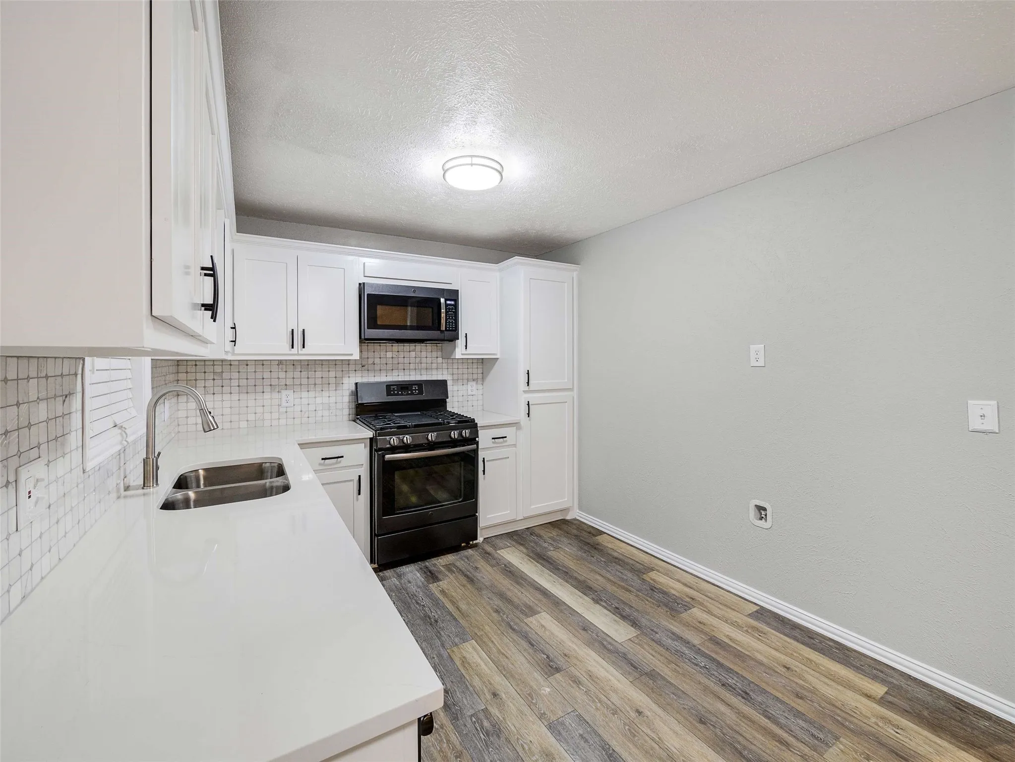 Kitchen featuring white cabinetry, solid-surface countertops, a tiled backsplash, wood-finish flooring, and black appliances
