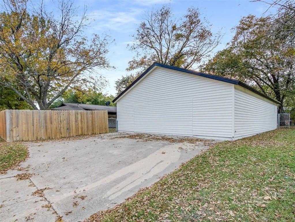 Detached structure featuring white horizontal siding, a gabled roof, concrete driveway, and wooden perimeter fencing