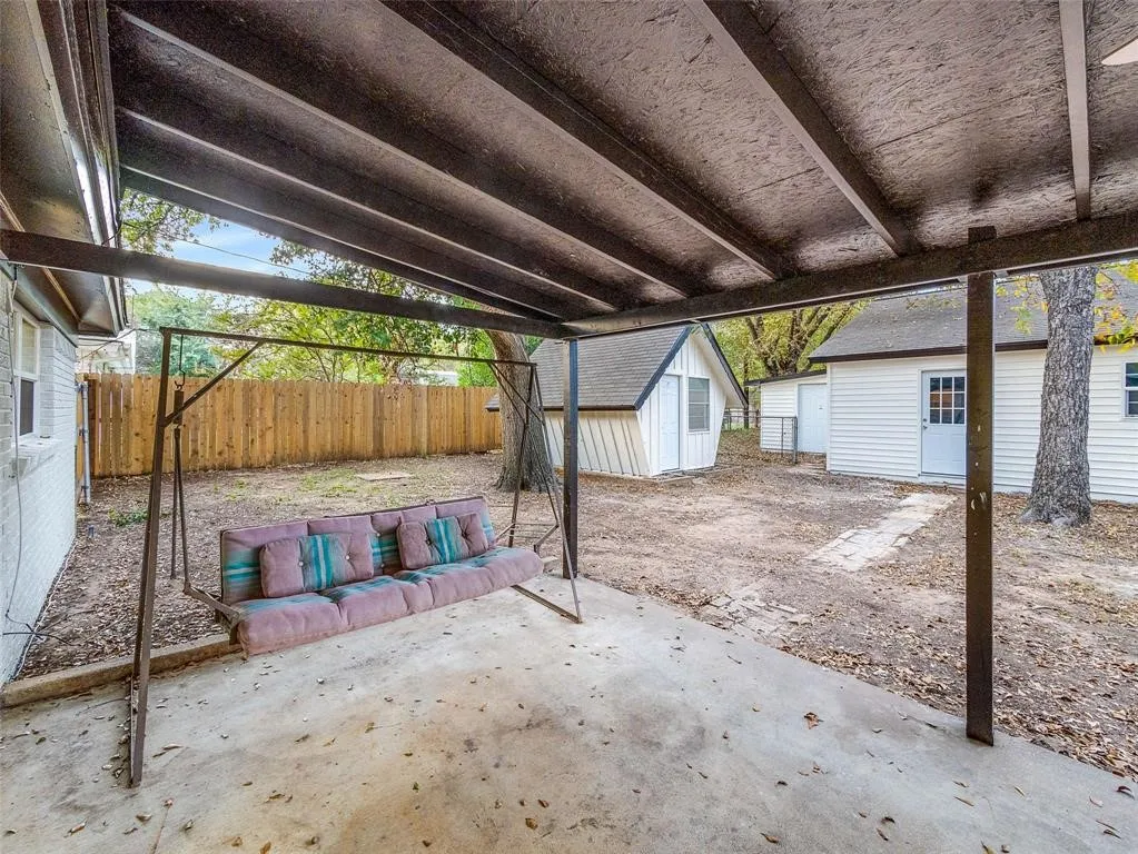 Covered concrete patio featuring a support beam structure, enclosed by a wood perimeter fence, inclusive of a detached storage outbuilding