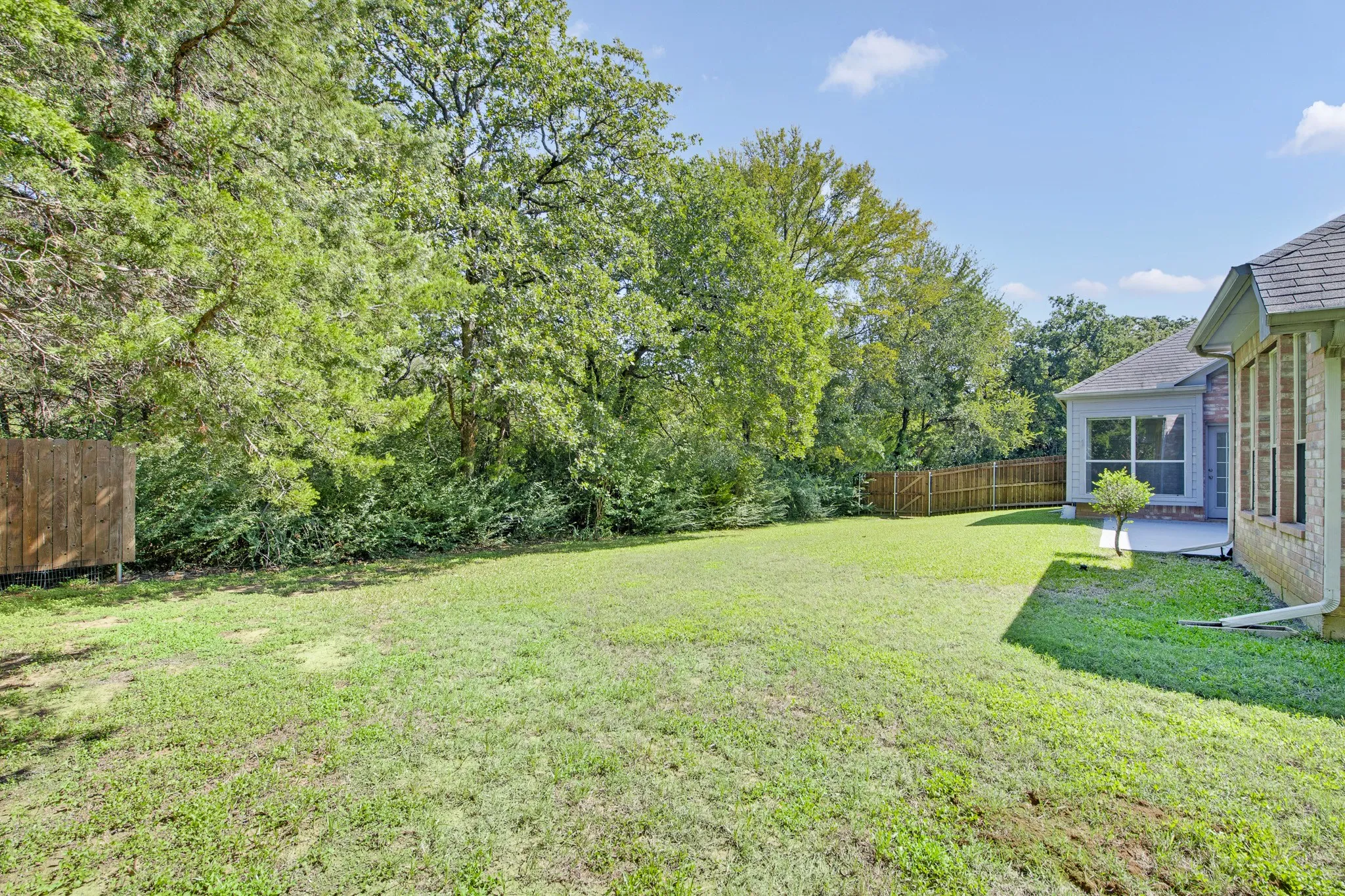 Rear yard featuring a grass lawn, mature trees, wood privacy fencing, and exterior brick masonry