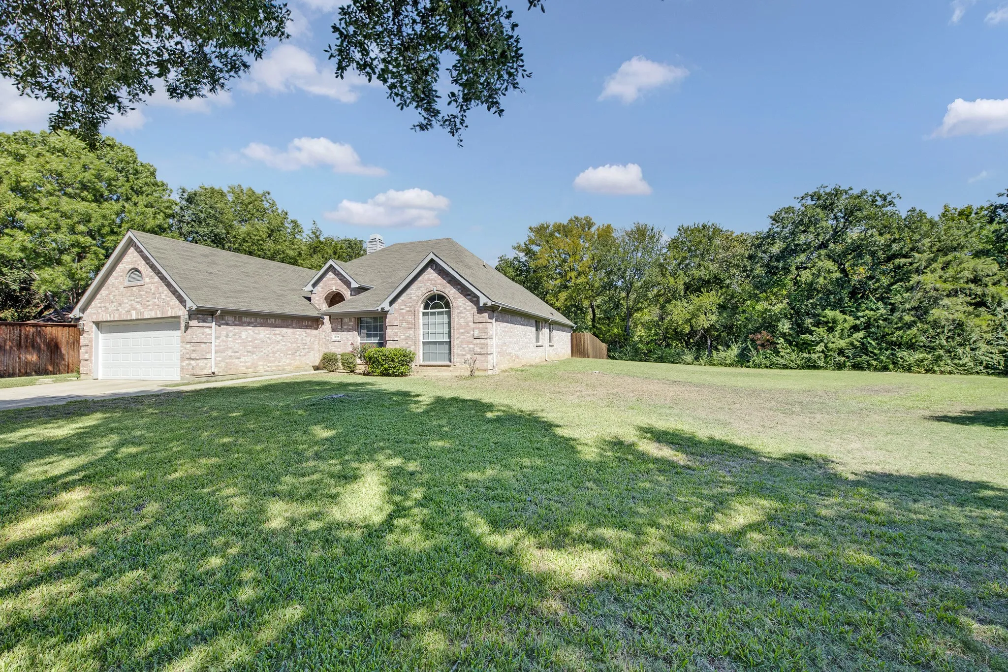 Brick exterior featuring a multi-gabled roofline, arched window detailing, and an attached two-car garage situated on a lot with mature trees