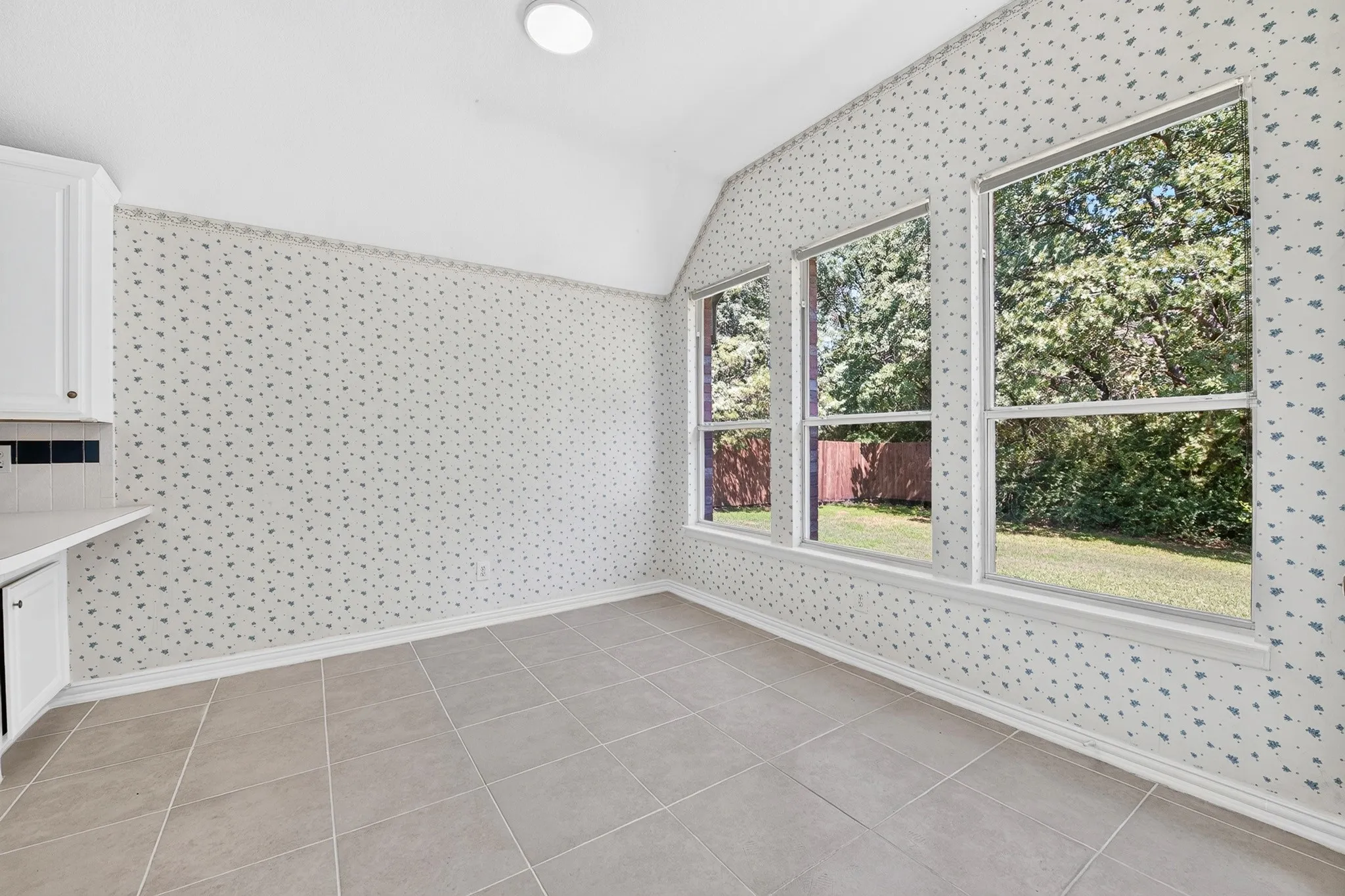 Room featuring large windows with outdoor exposure, vaulted ceilings, neutral tile flooring, and white cabinetry