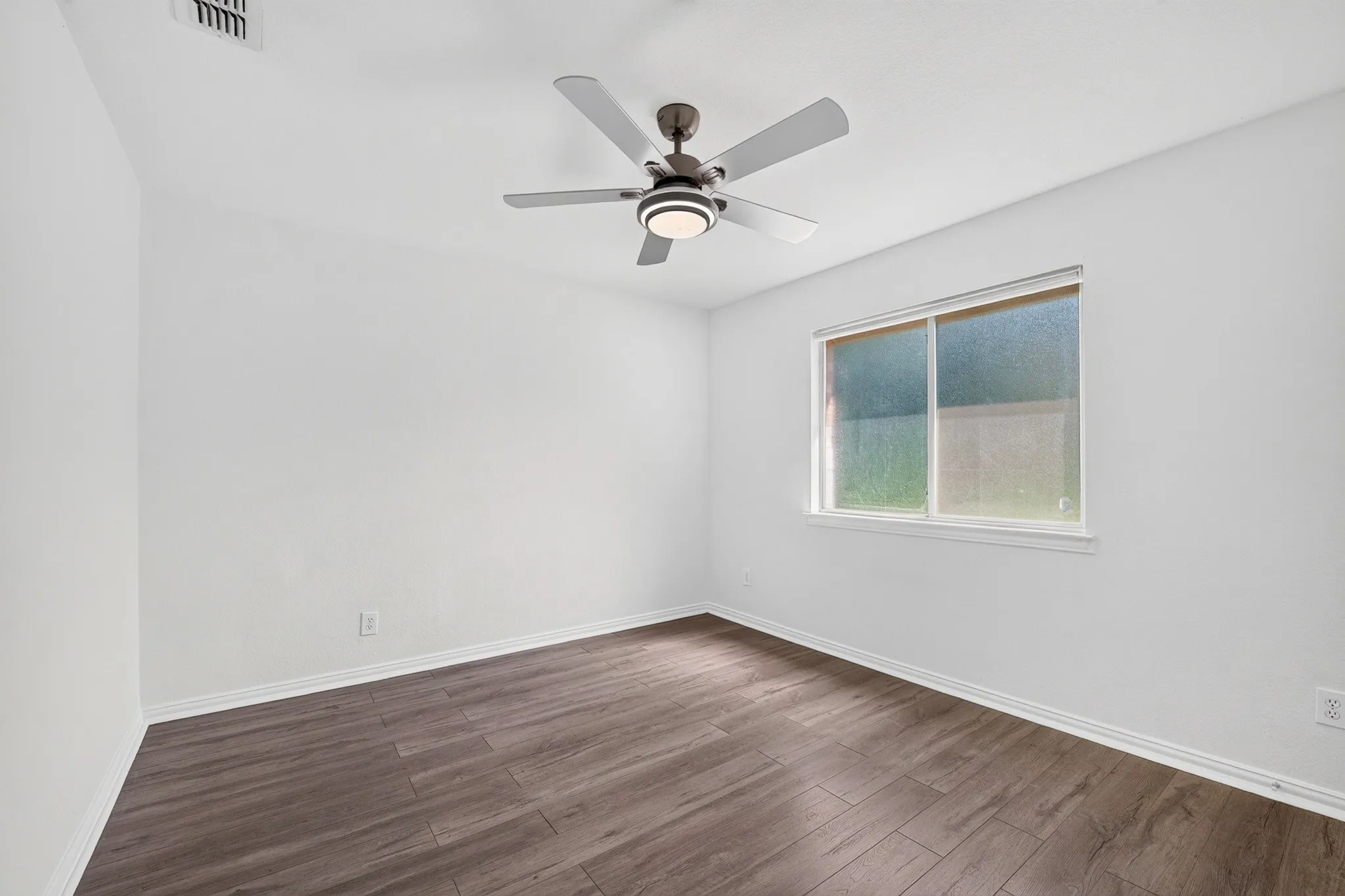 Room featuring wood-finish flooring, a matte-finish ceiling fan with integrated lighting, and a sliding window