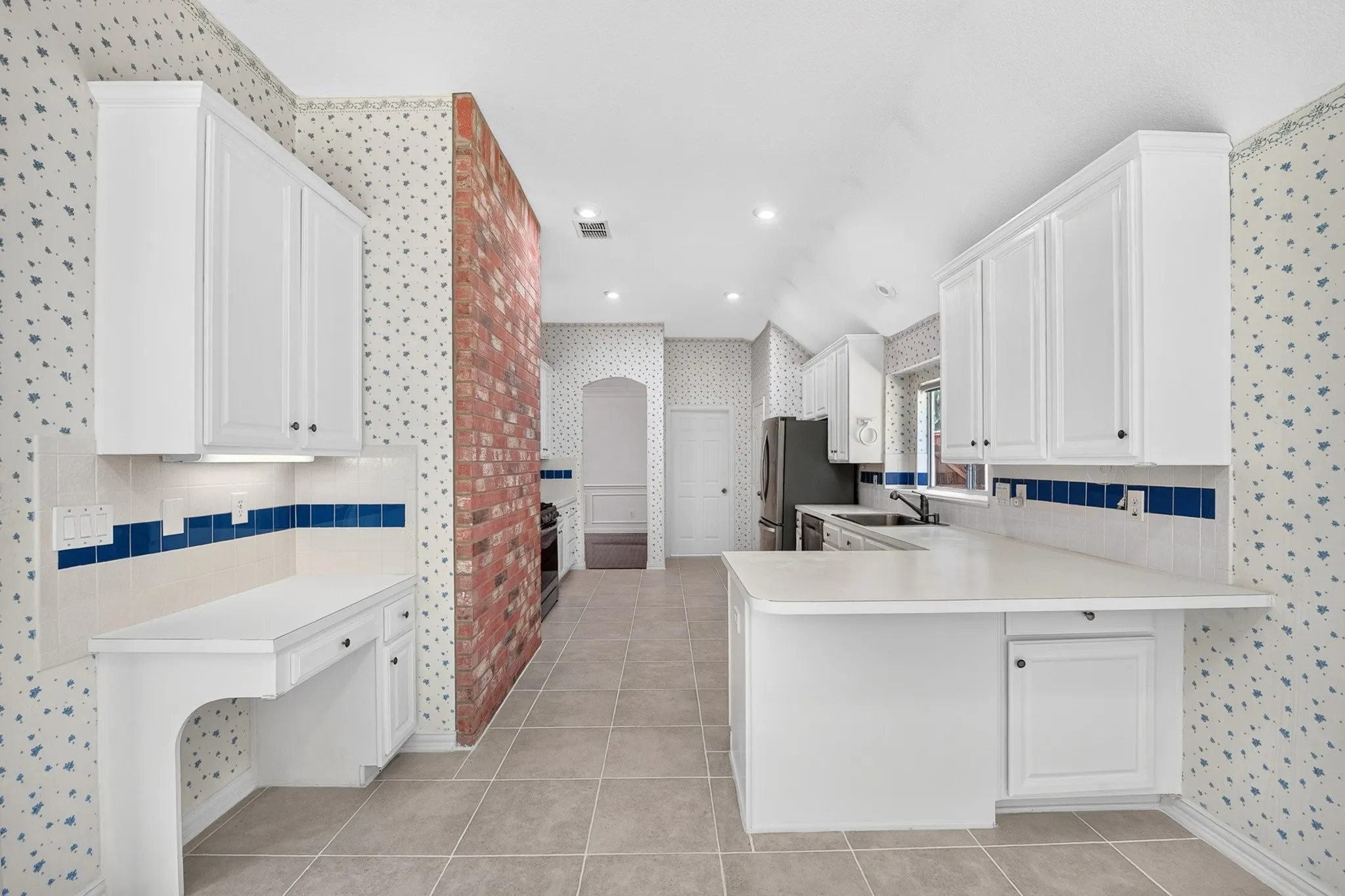 Kitchen featuring a brick accent wall, white cabinetry, integrated desk space, tiled flooring, and recessed lighting