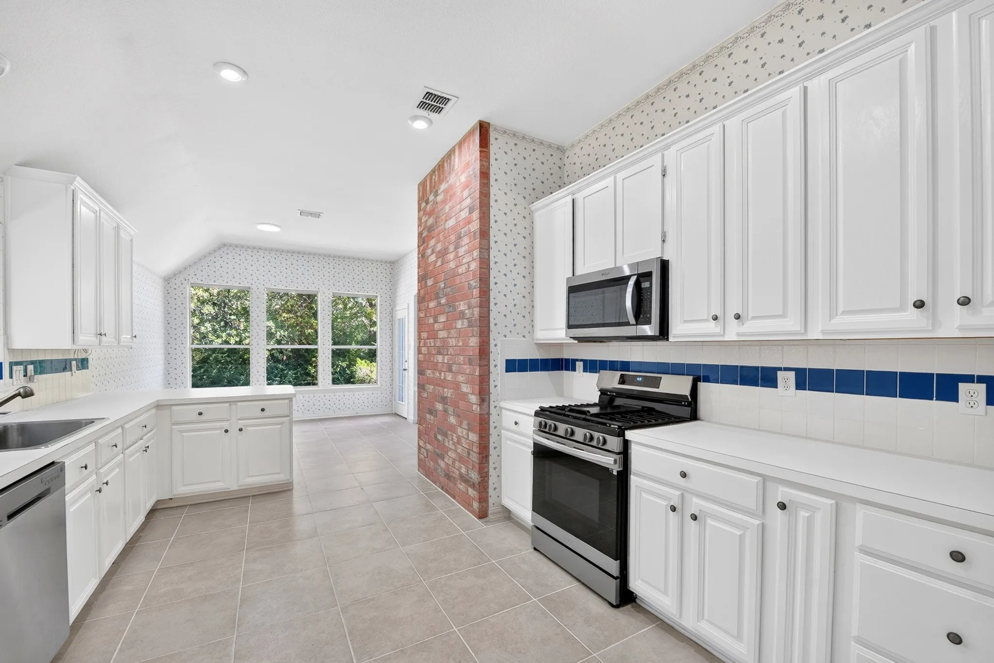 Kitchen featuring white cabinetry, stainless steel appliances, brick pillar accent, tile flooring, and multi-pane windows