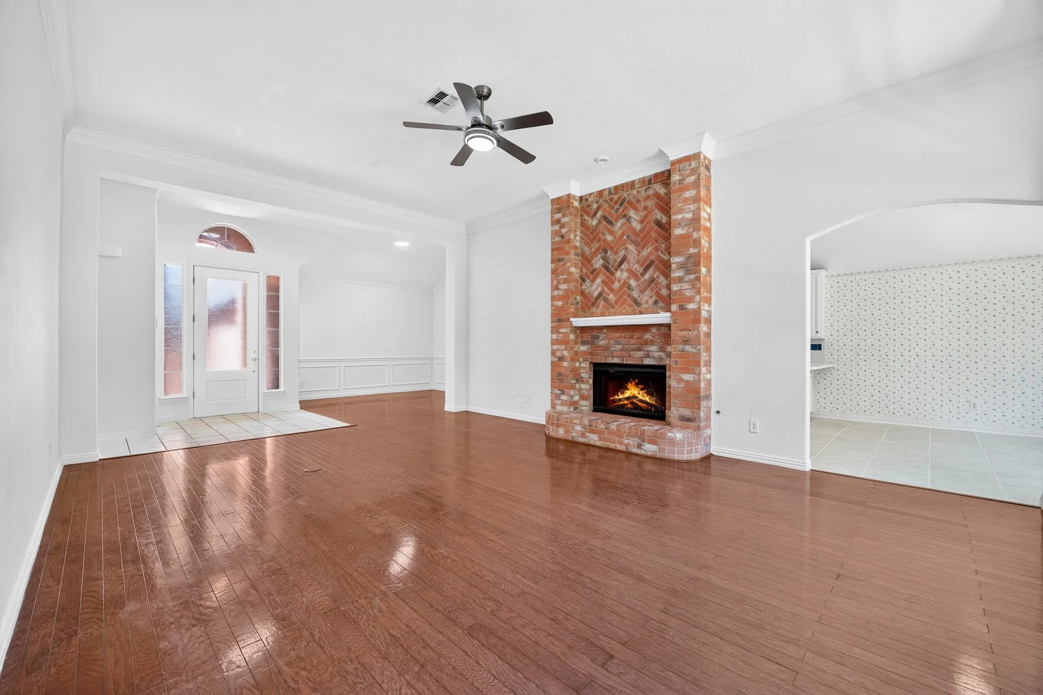 Open-concept interior featuring wood-finish flooring, a floor-to-ceiling brick fireplace with a herringbone pattern inlay, and crown molding