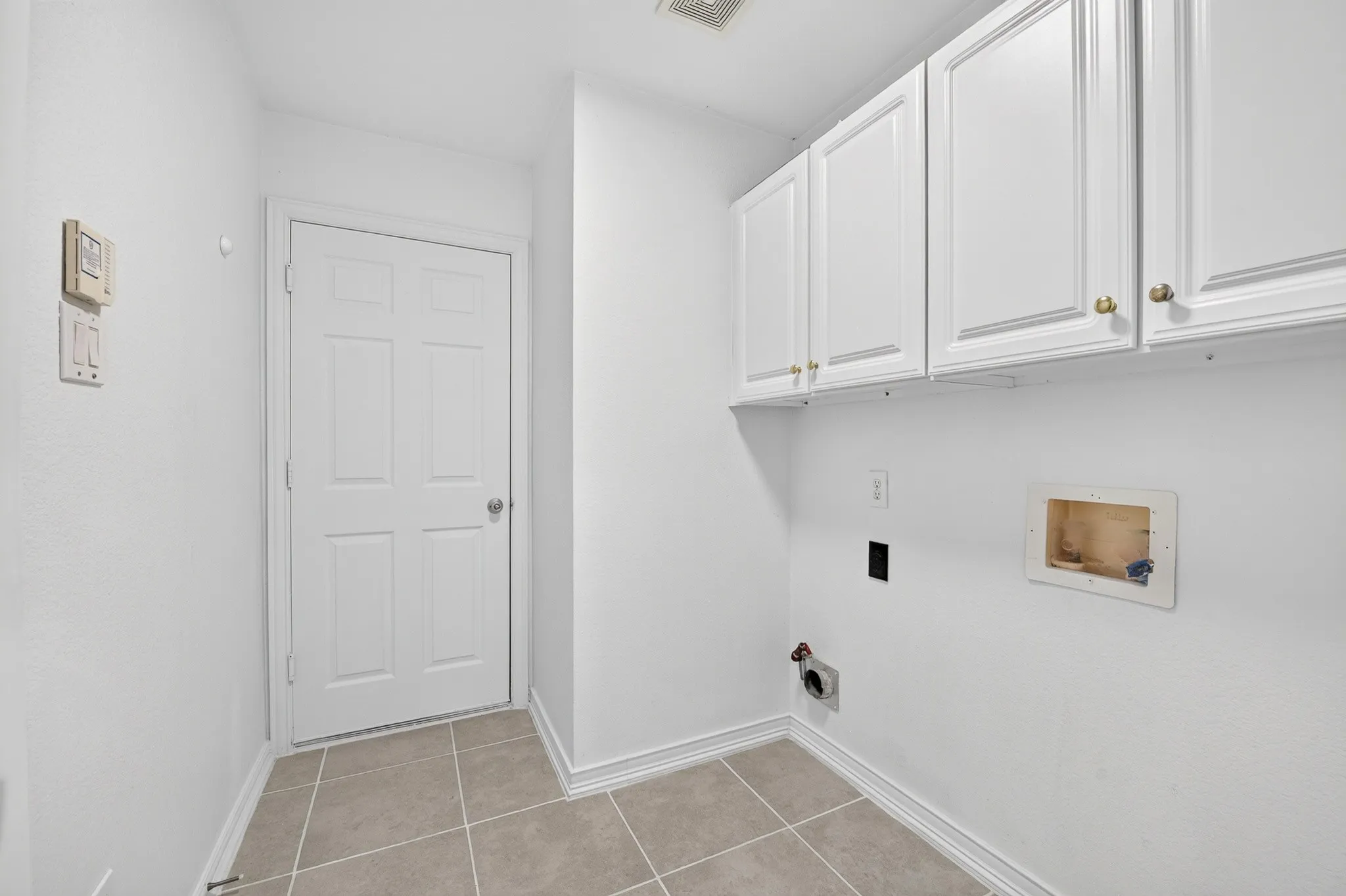 Utility area featuring white shaker-style wall cabinetry, neutral-toned square tile flooring, and a solid-core six-panel door