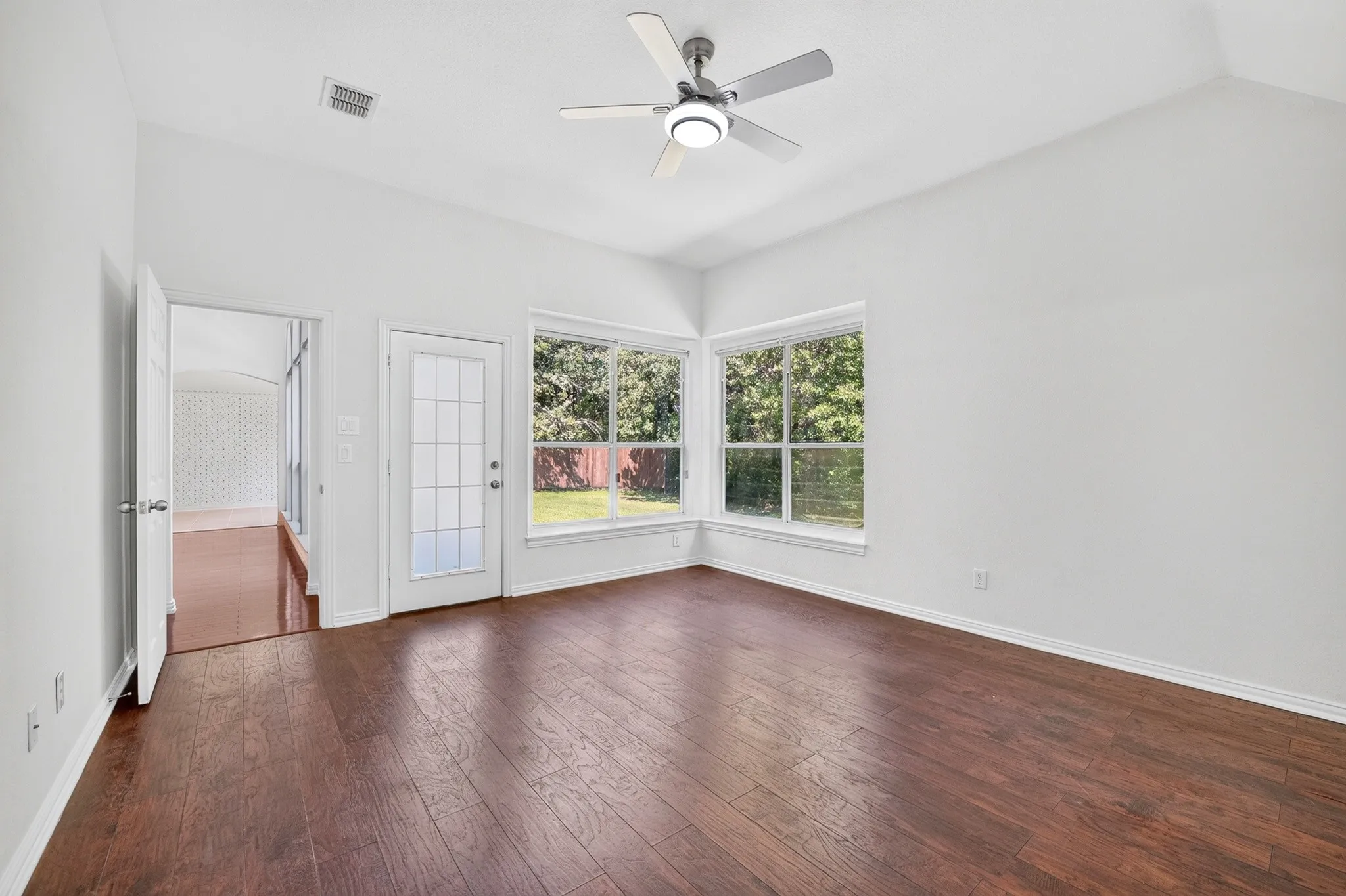 Room featuring vaulted ceilings, wood-finish flooring, a central ceiling fan with integrated lighting, and multiple windows