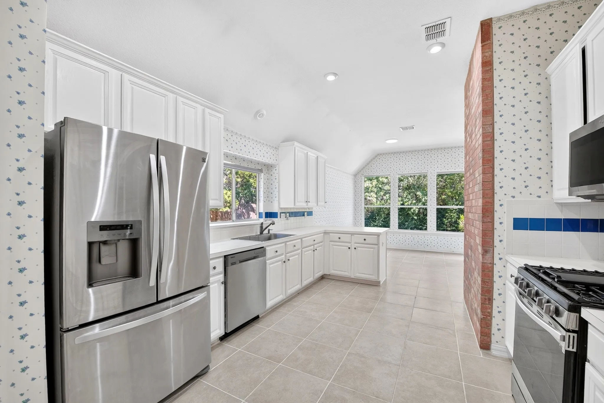 Kitchen featuring white cabinetry, stainless steel appliances, tile flooring, and an exposed brick column