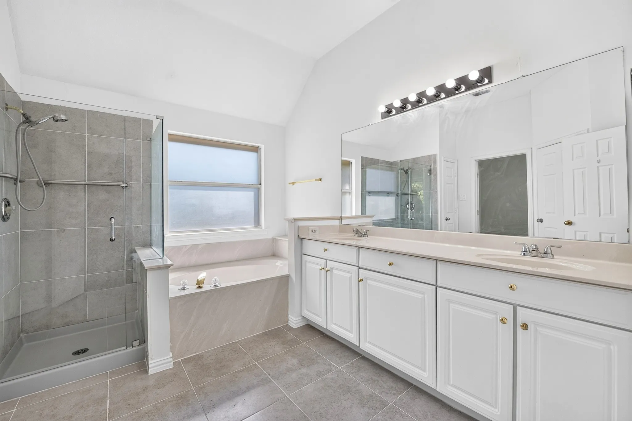 Bathroom featuring a glass-enclosed shower with gray tiling, built-in soaking tub, dual-sink vanity with solid surface countertops, and vaulted ceiling