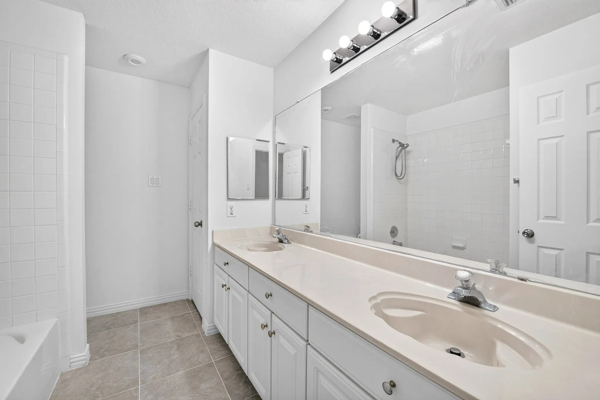 Bathroom featuring a dual-sink vanity with solid-surface countertops, full-width vanity mirror, tile flooring, and a shower-tub combination with tiled surround