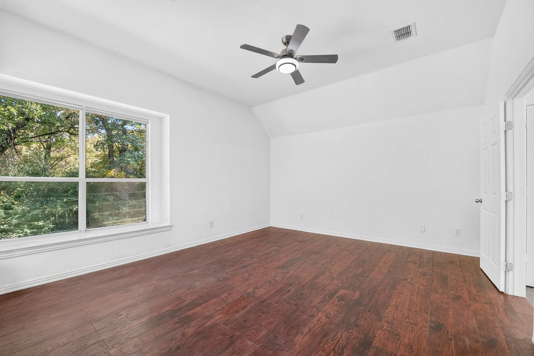 Room featuring vaulted ceilings, wood-finish flooring, a large picture window, and a ceiling fan with integrated lighting