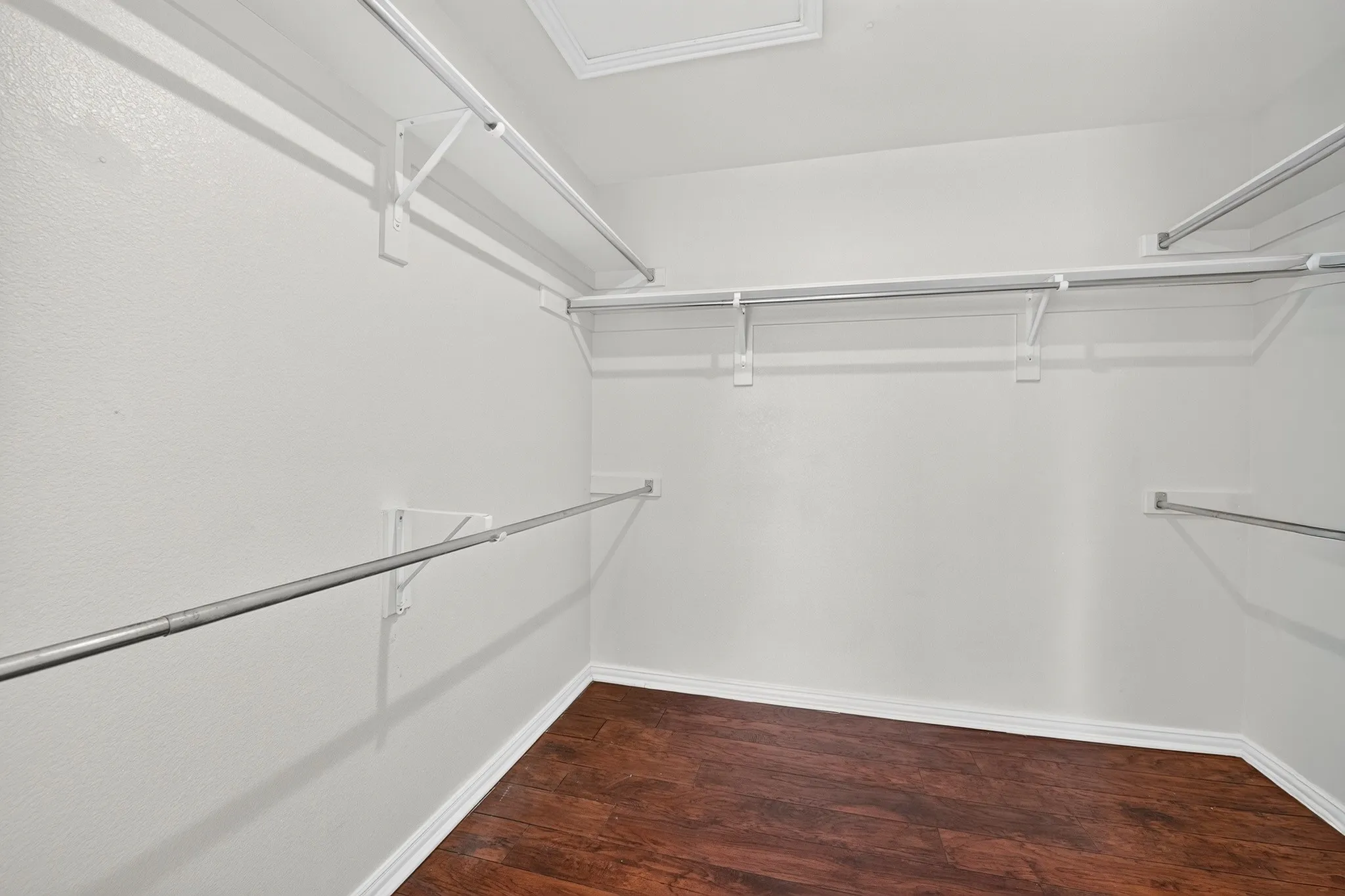 Walk-in storage space featuring wood-finish flooring and tiered metal shelving rods