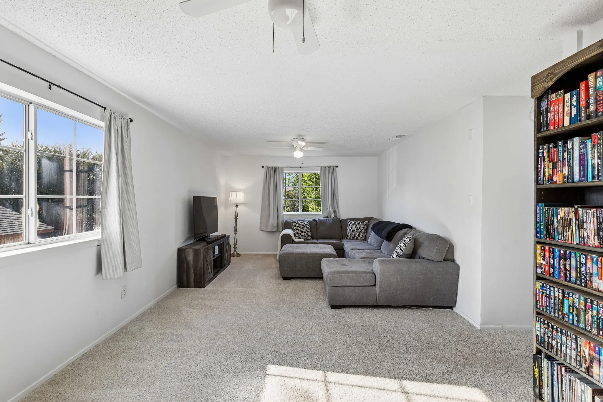 Living space featuring neutral carpeting, dual ceiling fans, and multiple windows providing natural light