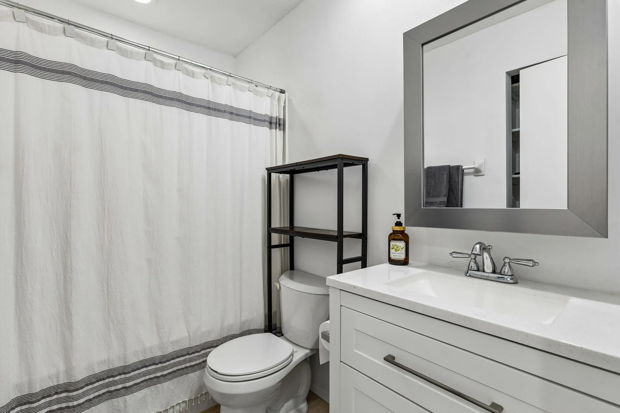 White vanity with a solid surface countertop, rectangular integrated sink, polished metal faucet, and framed rectangular mirror
