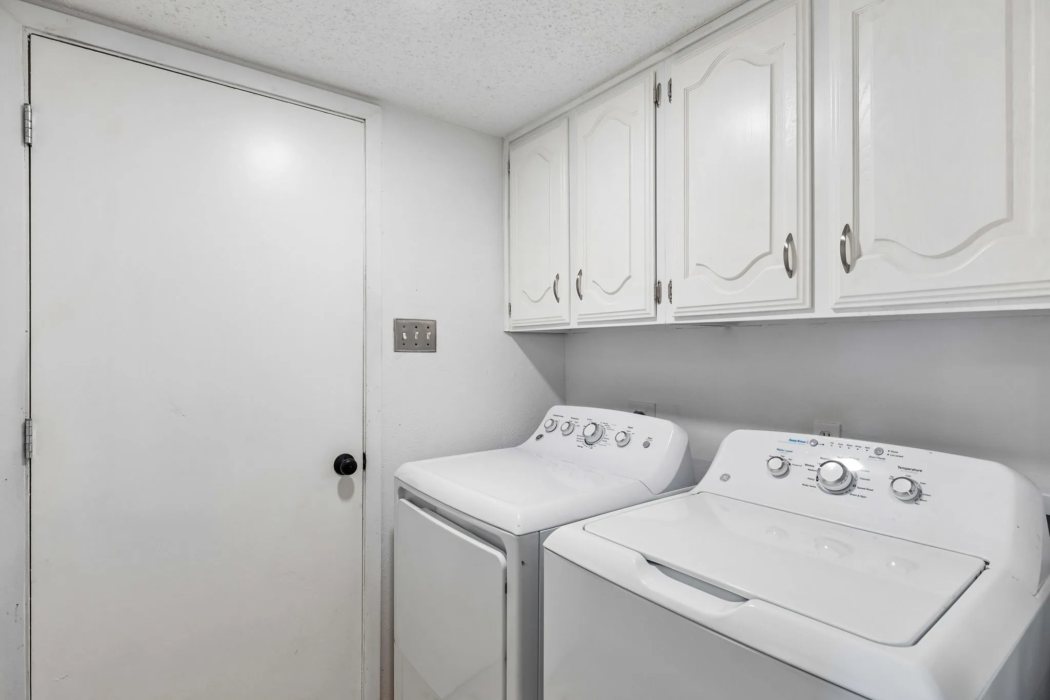 Laundry area featuring white raised-panel upper cabinetry, a solid-core interior door with matte black hardware, and dedicated appliance hookups