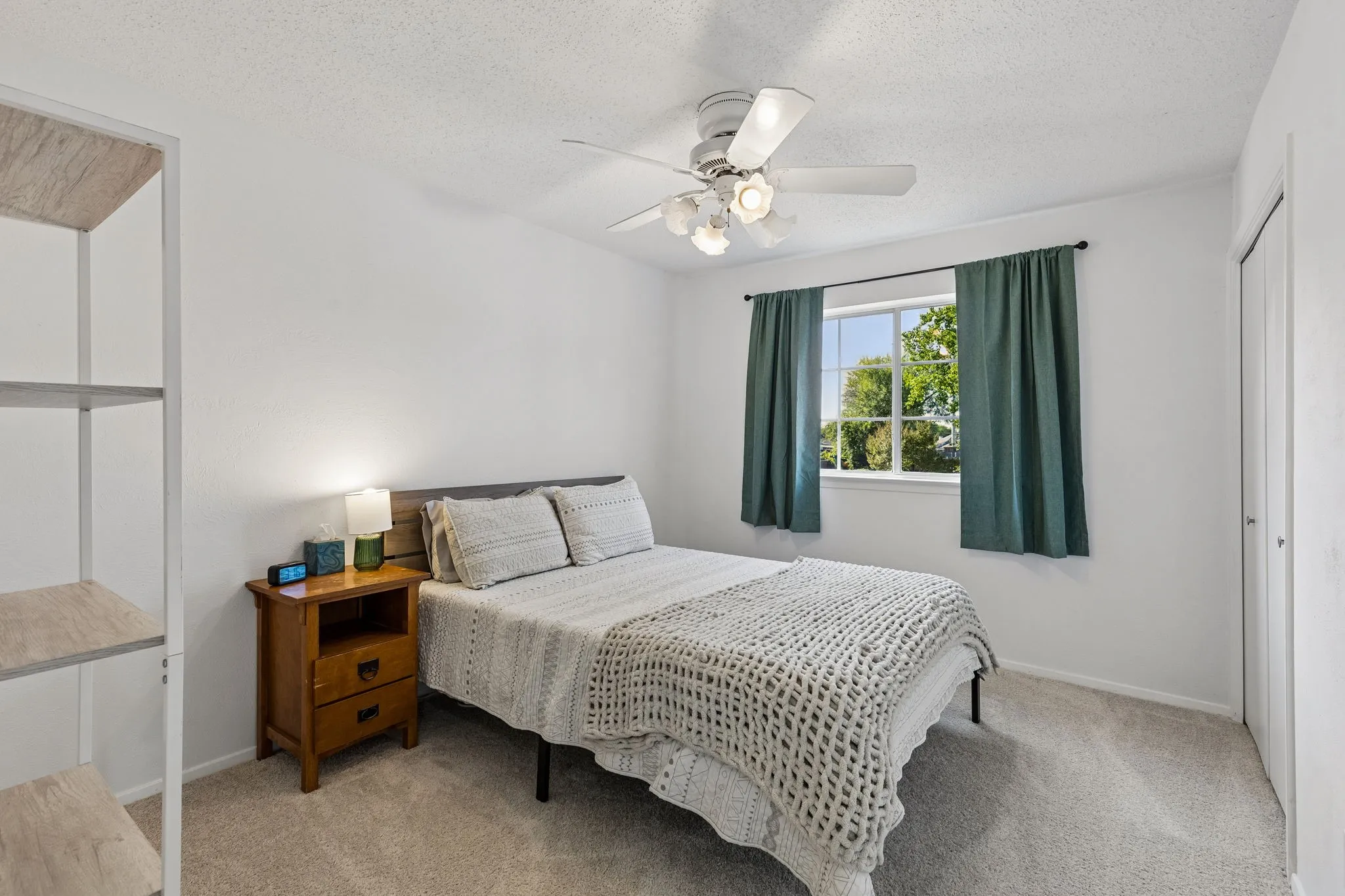 White-toned walls, ceiling-mounted multi-light fan, window with exterior grid, neutral carpeting, and a double-door closet