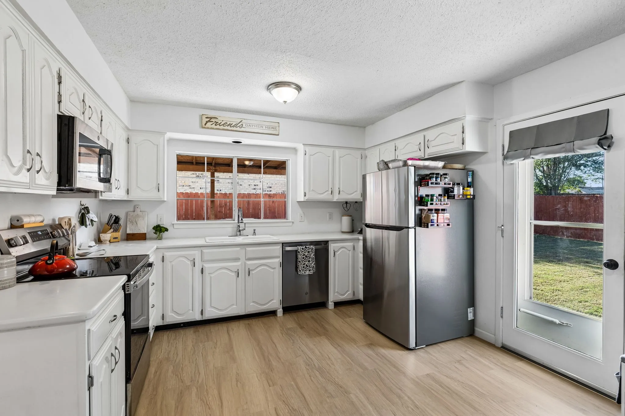 Kitchen featuring white cabinetry, stainless steel appliances, wood-finish flooring, a double-basin sink, and glass-paneled exterior door